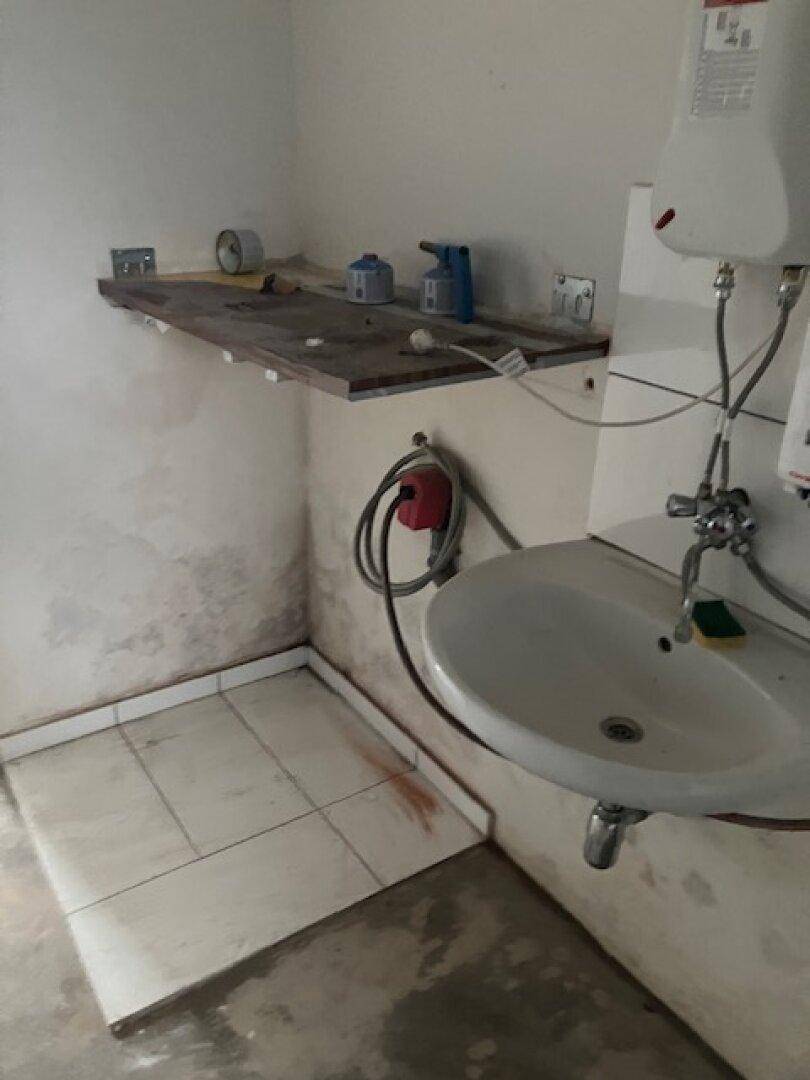Hauswirtschaftsraum mit Waschbecken, Warmwasserbereiter und einem kleinen gefliesten Bereich am Boden.