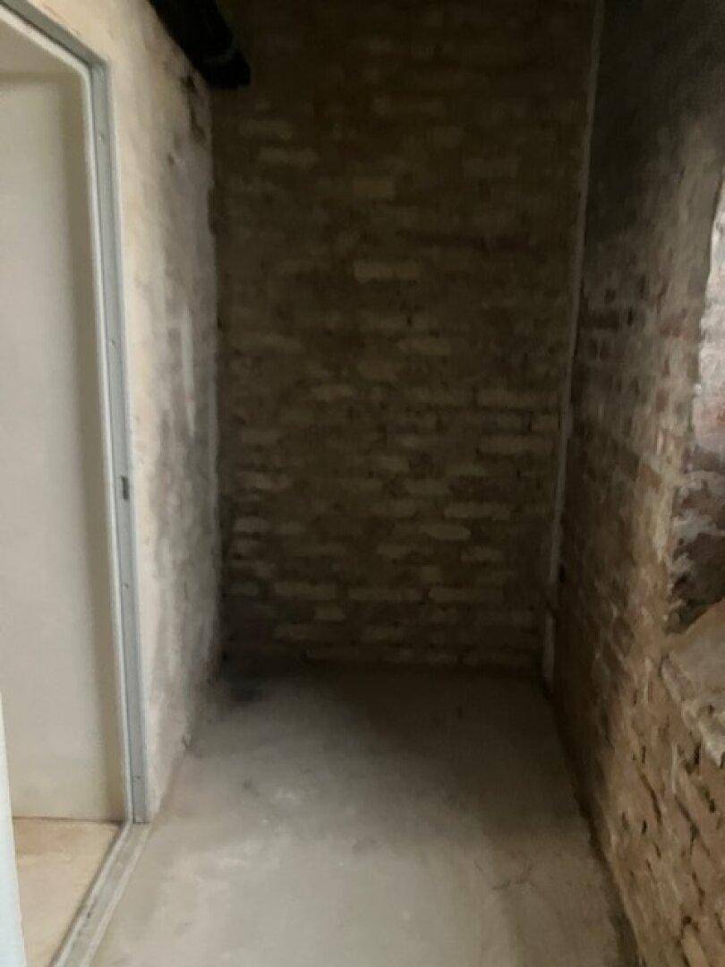 Weiterer schmaler Abstellraum mit Ziegelwänden und einem einfachen Betonboden.