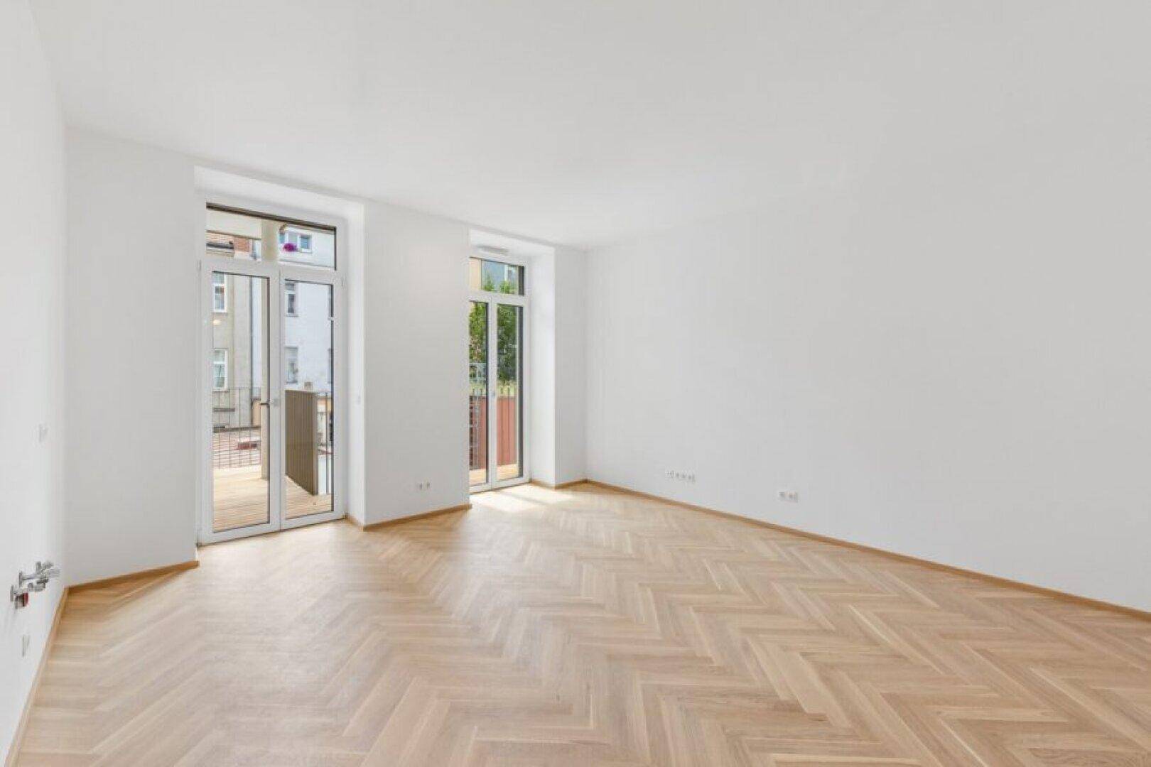 Heller, leerer Raum mit Fischgrätparkett und zwei französischen Balkonen, bereit zur Gestaltung.