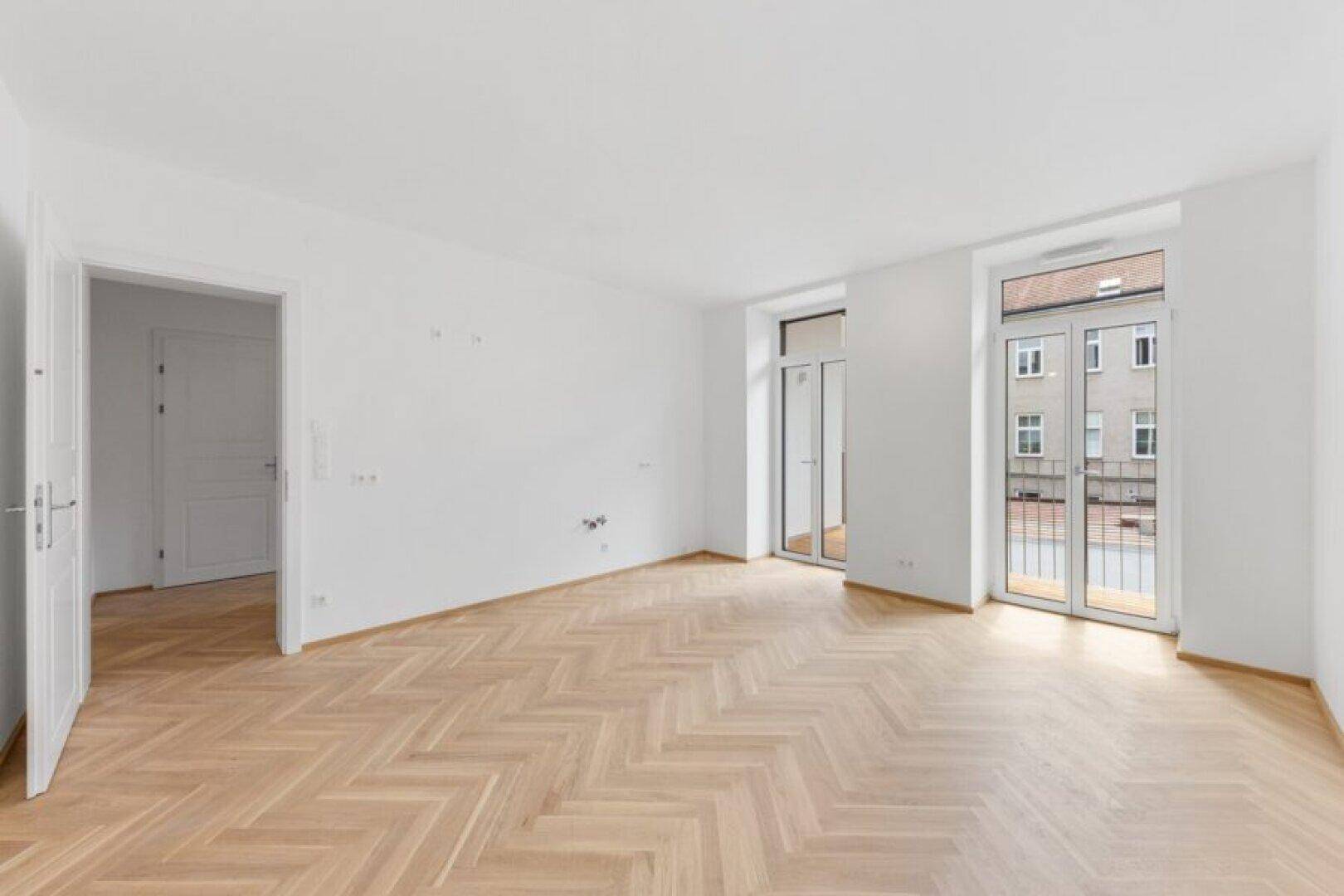 Geräumiger, heller Raum mit Fischgrätparkett und Zugang zu einem französischen Balkon.