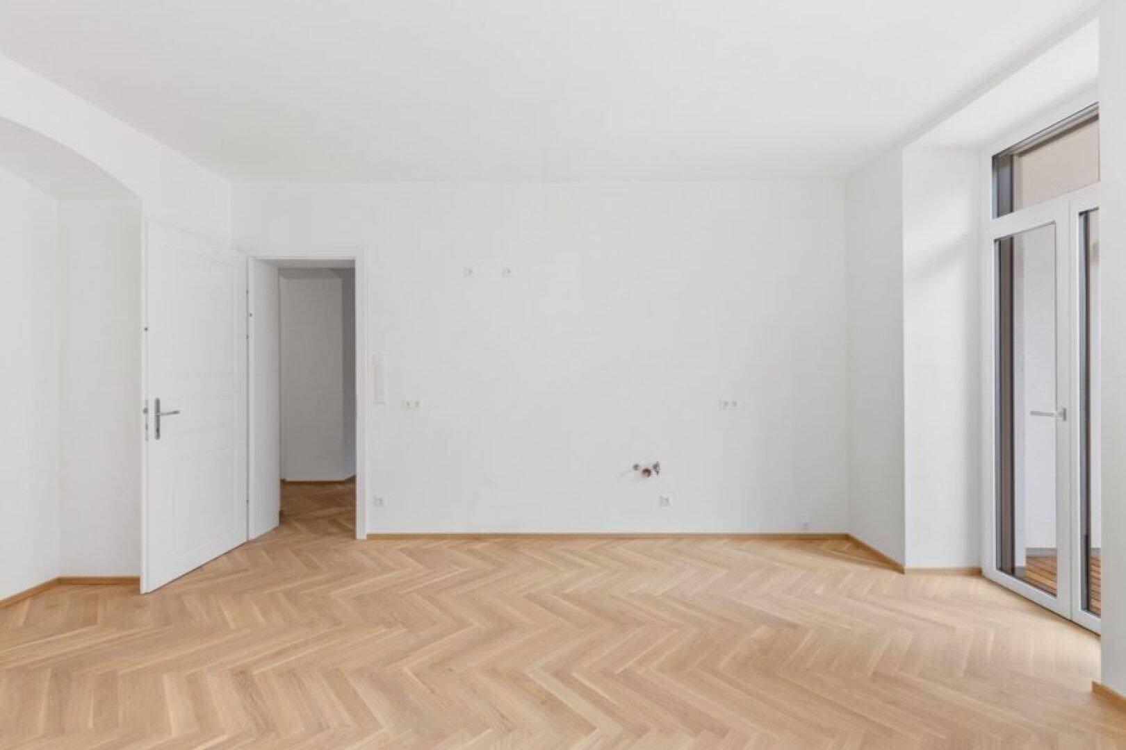 Lichtdurchfluteter Raum mit elegantem Fischgrätparkett und einem französischen Balkon.