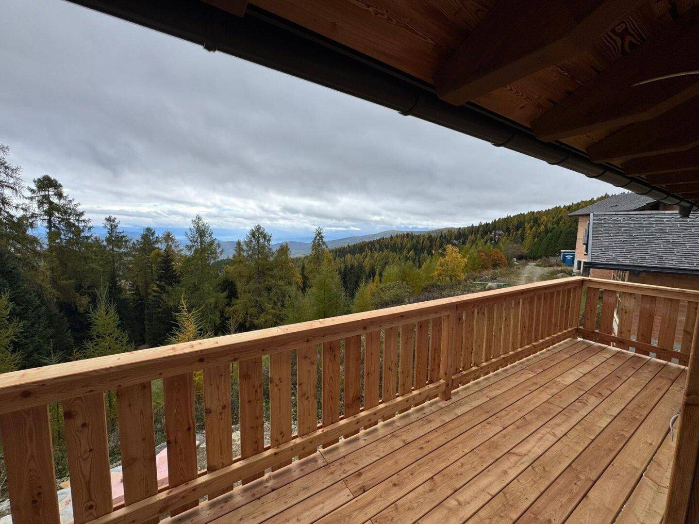 Geräumiger Holzbalkon mit Geländer und Panoramablick auf die umliegenden Wälder und Berge.