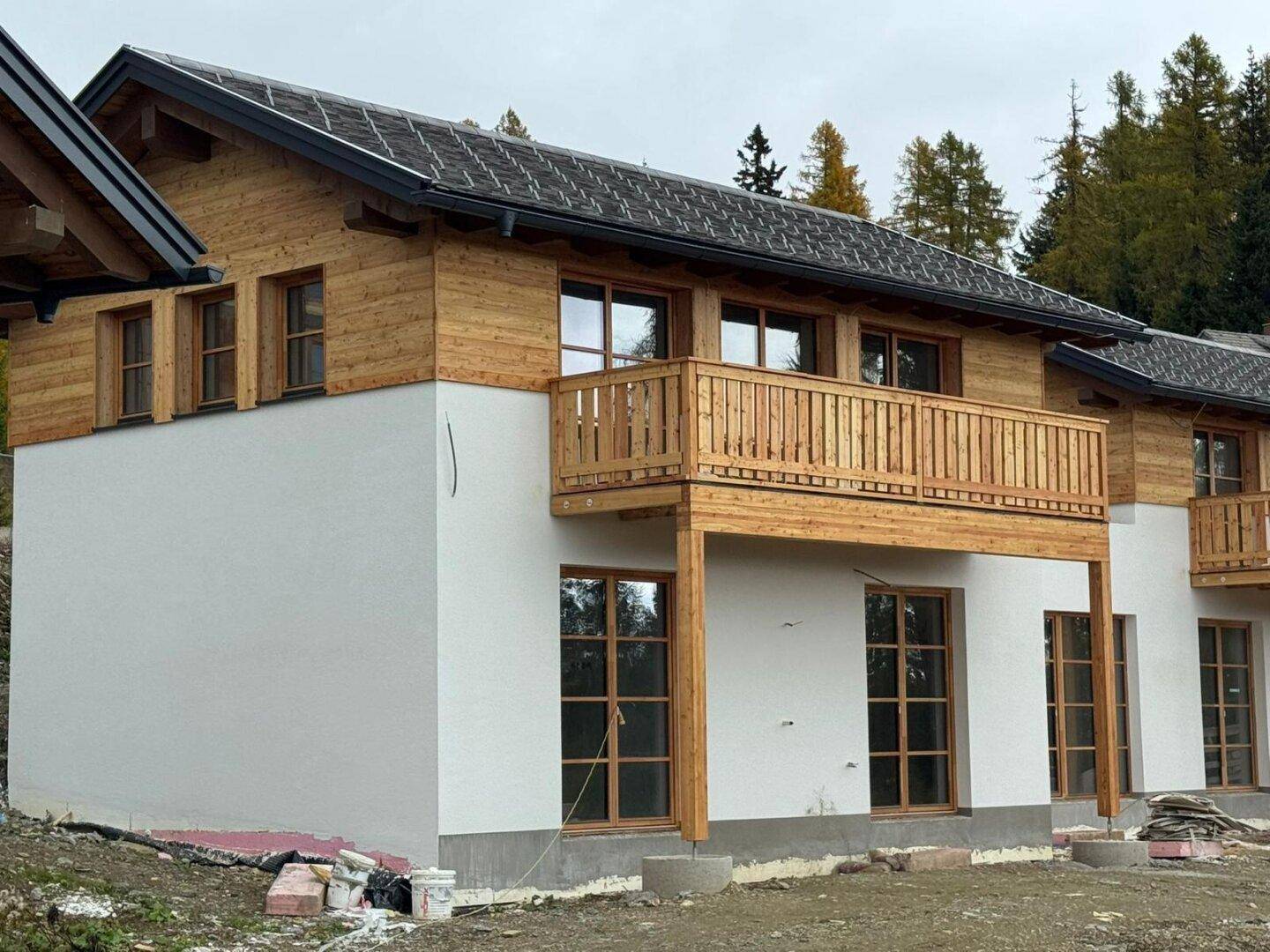 Seitenansicht eines neuen Chalets mit Holzverkleidung und Balkon, eingebettet in eine natürliche Umgebung.