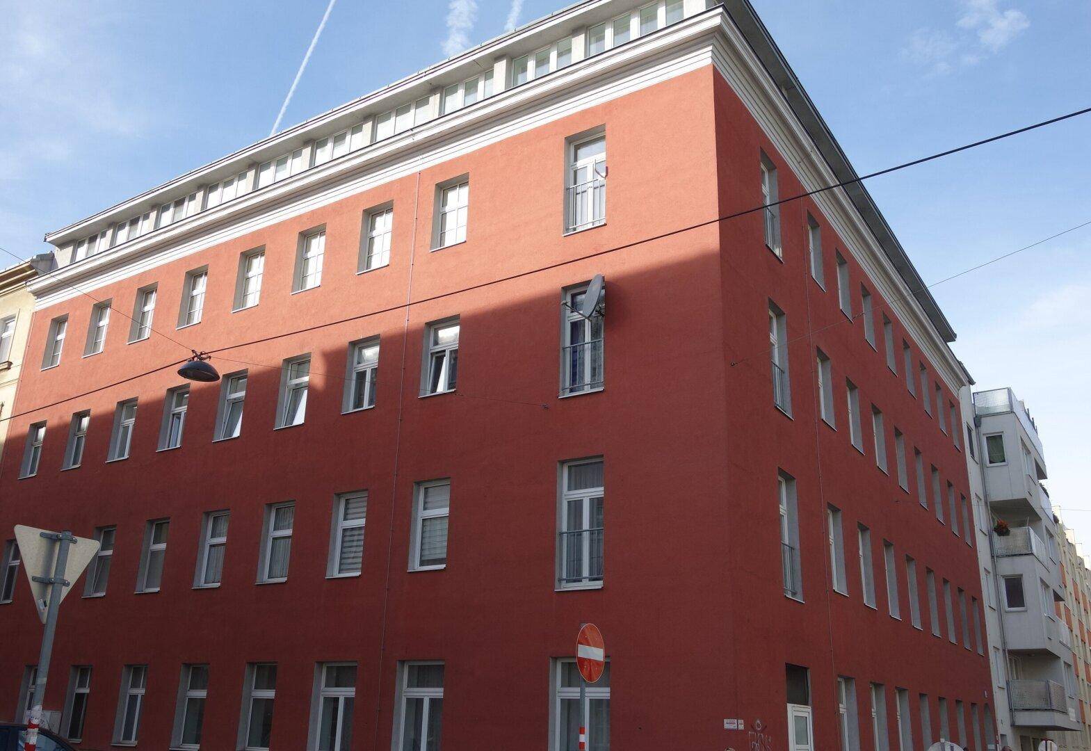 Mehrstöckiges Gebäude mit markanter roter Fassade und zahlreichen Fenstern an einer Straßenecke.