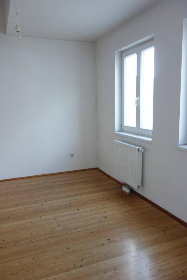 Einfaches Zimmer mit hellem Holzfußboden und einem Fenster, ideal als Schlaf- oder Kinderzimmer.