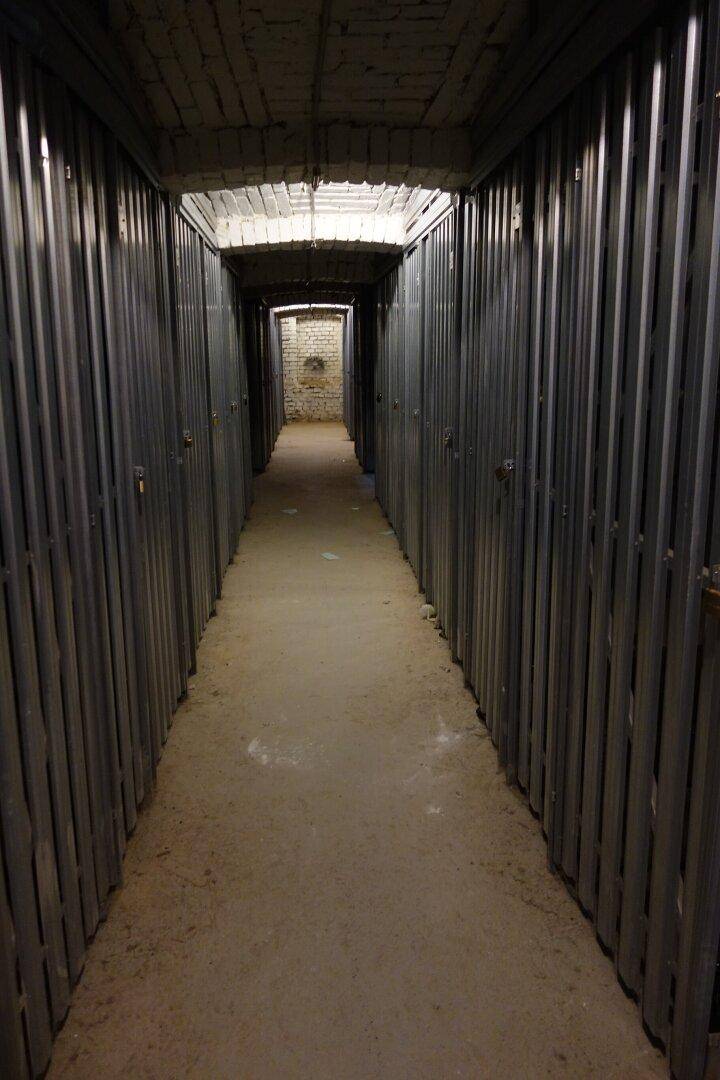 Langer, schmaler Kellergang mit zahlreichen Lagerabteilen aus Metall.