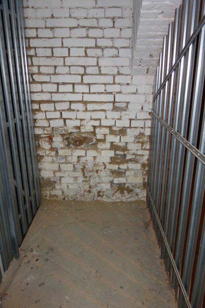 Ecke eines Kellerabteils mit freigelegter, weiß gestrichener Ziegelwand und Metallabtrennungen.