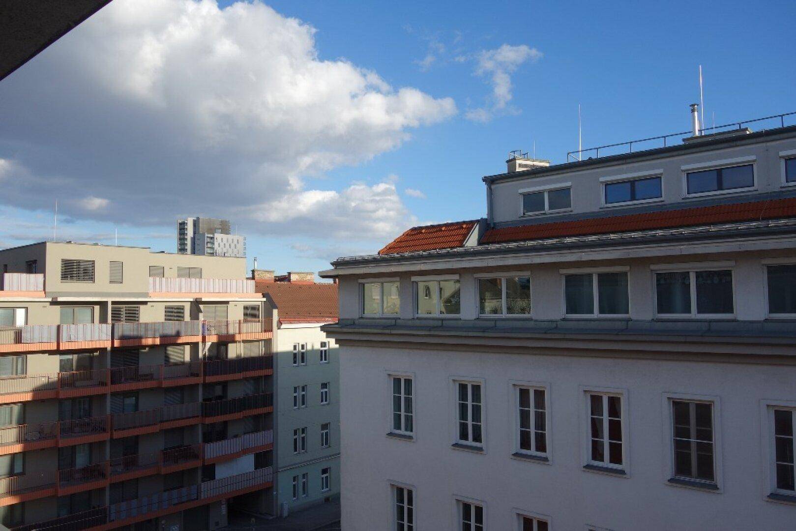 Außenansicht von Wohngebäuden mit Dächern und Balkonen unter blauem Himmel mit Wolken.