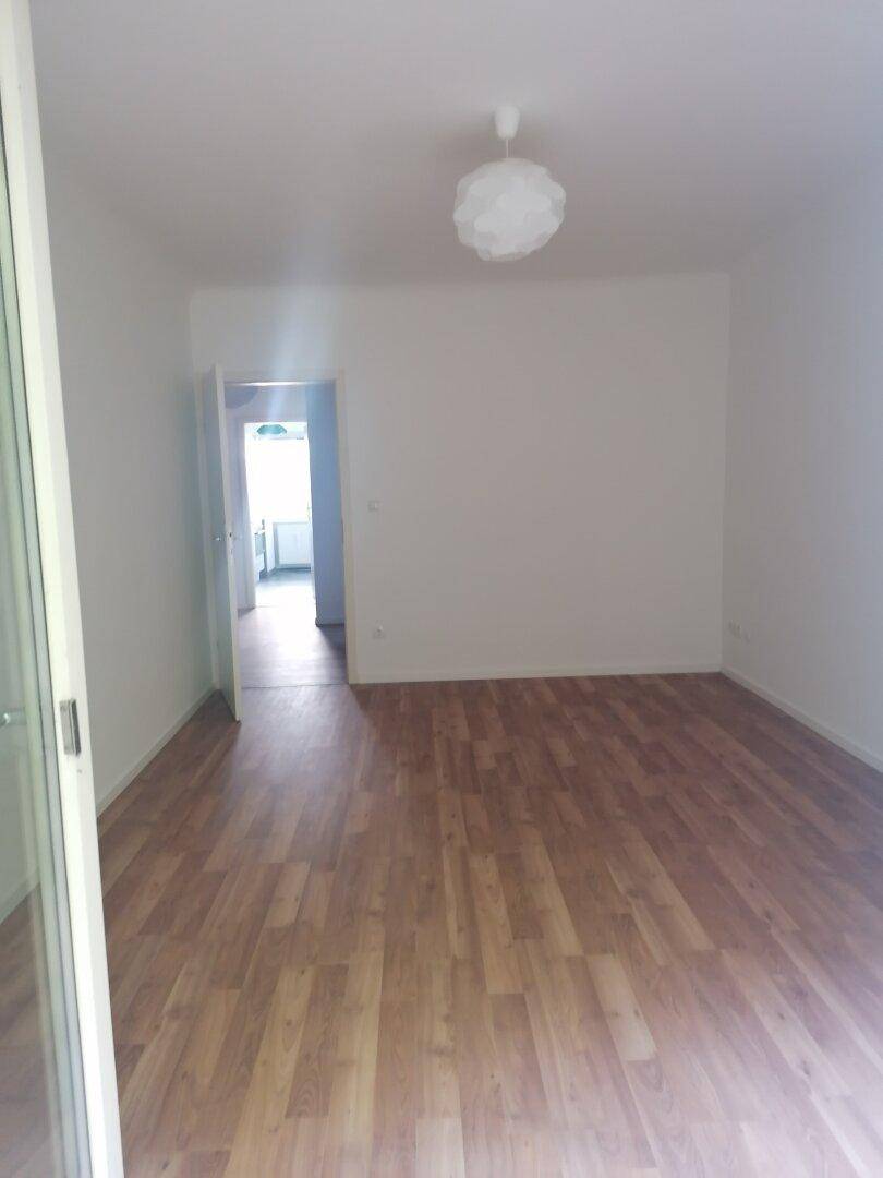 Heller, leerer Wohnraum mit Laminatboden, weißen Wänden und Zugang zu weiteren Zimmern.