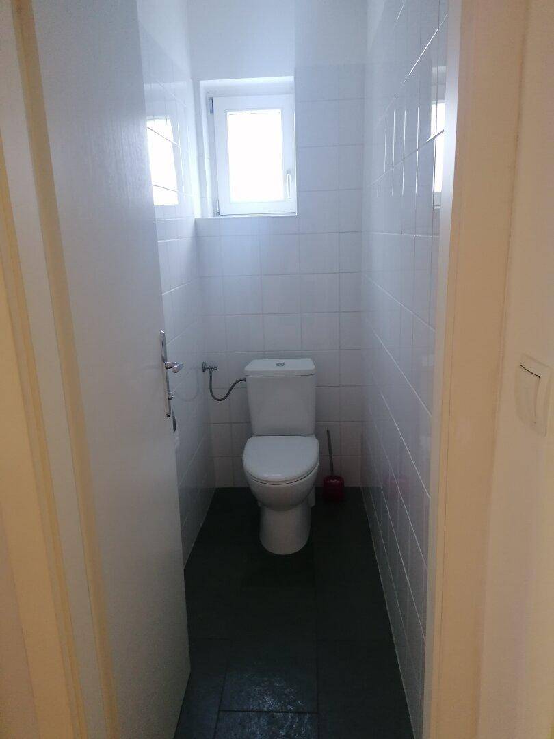 Separates WC mit Toilette, Fenster und weißen Fliesen, in einem sauberen Zustand.