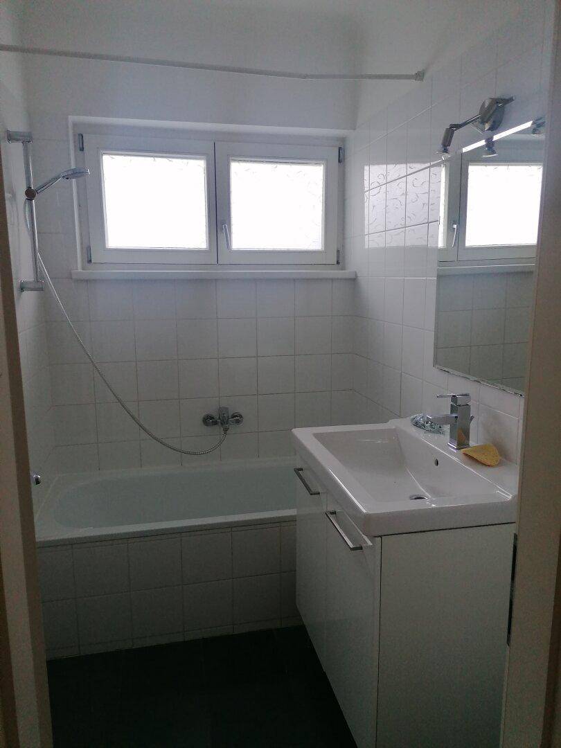 Funktionales Badezimmer mit Badewanne, Duschvorrichtung und Waschbecken mit Spiegelschrank.
