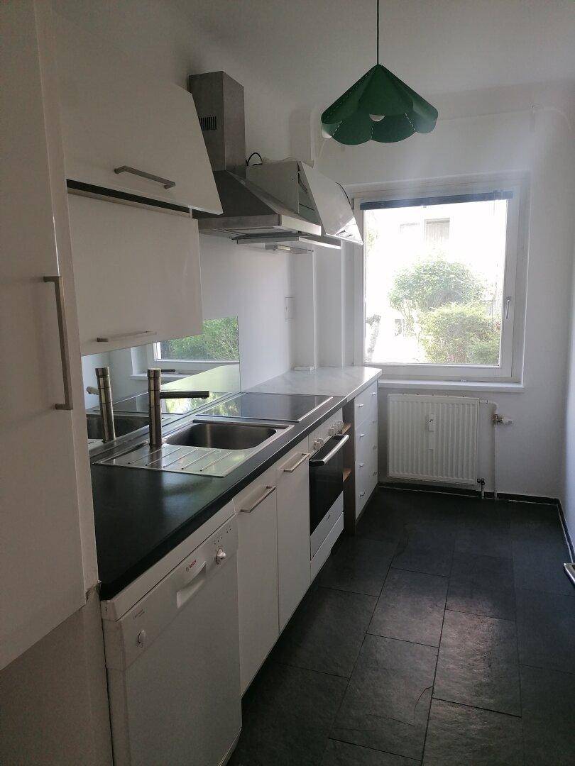 Funktionale Küche mit weißen Schränken, dunkler Arbeitsplatte, Spüle und Fenster.