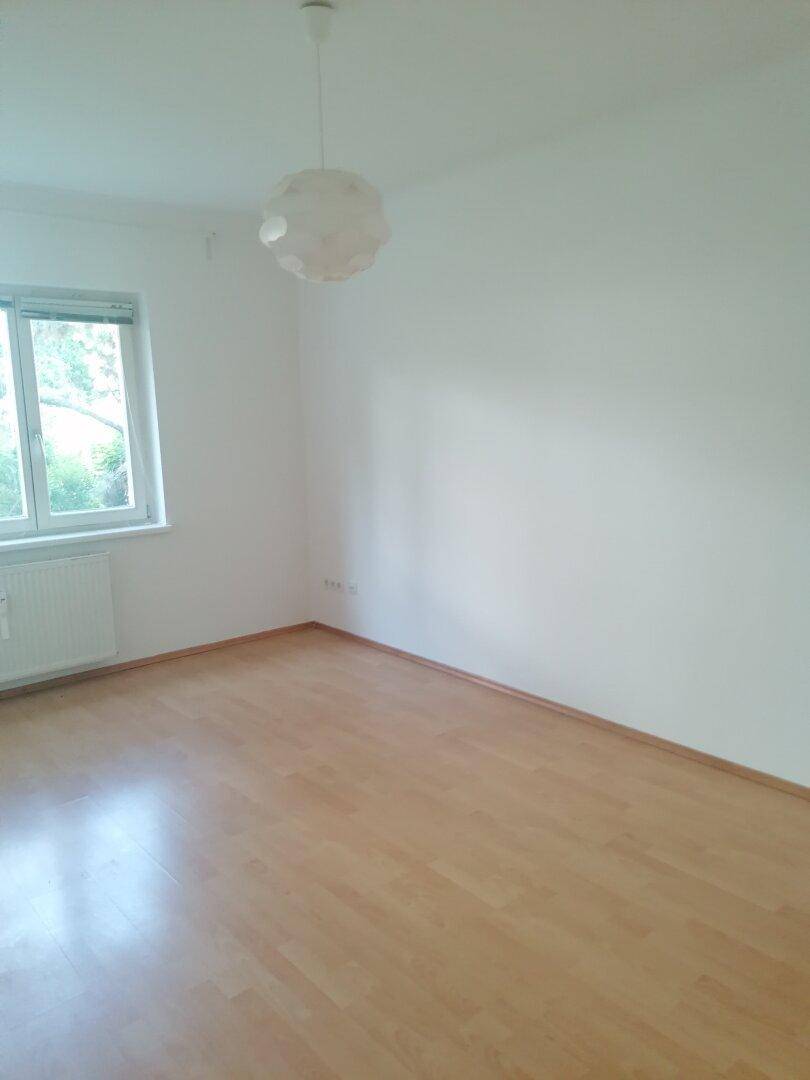 Leeres Schlafzimmer mit Laminatboden, weißen Wänden und einem Fenster für Tageslicht.
