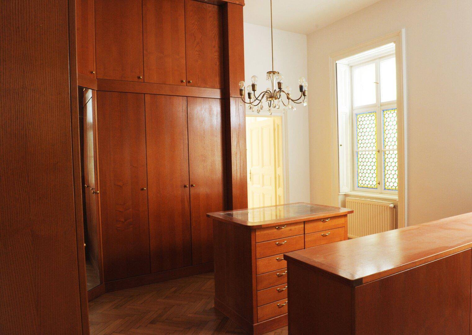Schlafzimmer mit maßgefertigten Holzschränken, Kommoden und einem Fenster mit Buntglaselementen.