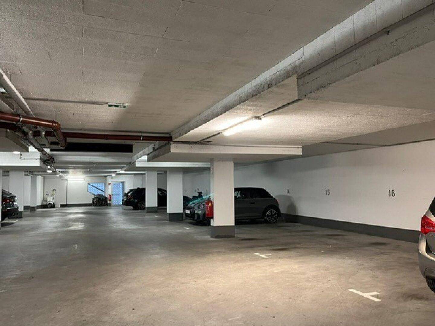 Weitläufige Tiefgarage mit nummerierten Stellplätzen, Betonstützen und sichtbaren Installationen an der Decke.