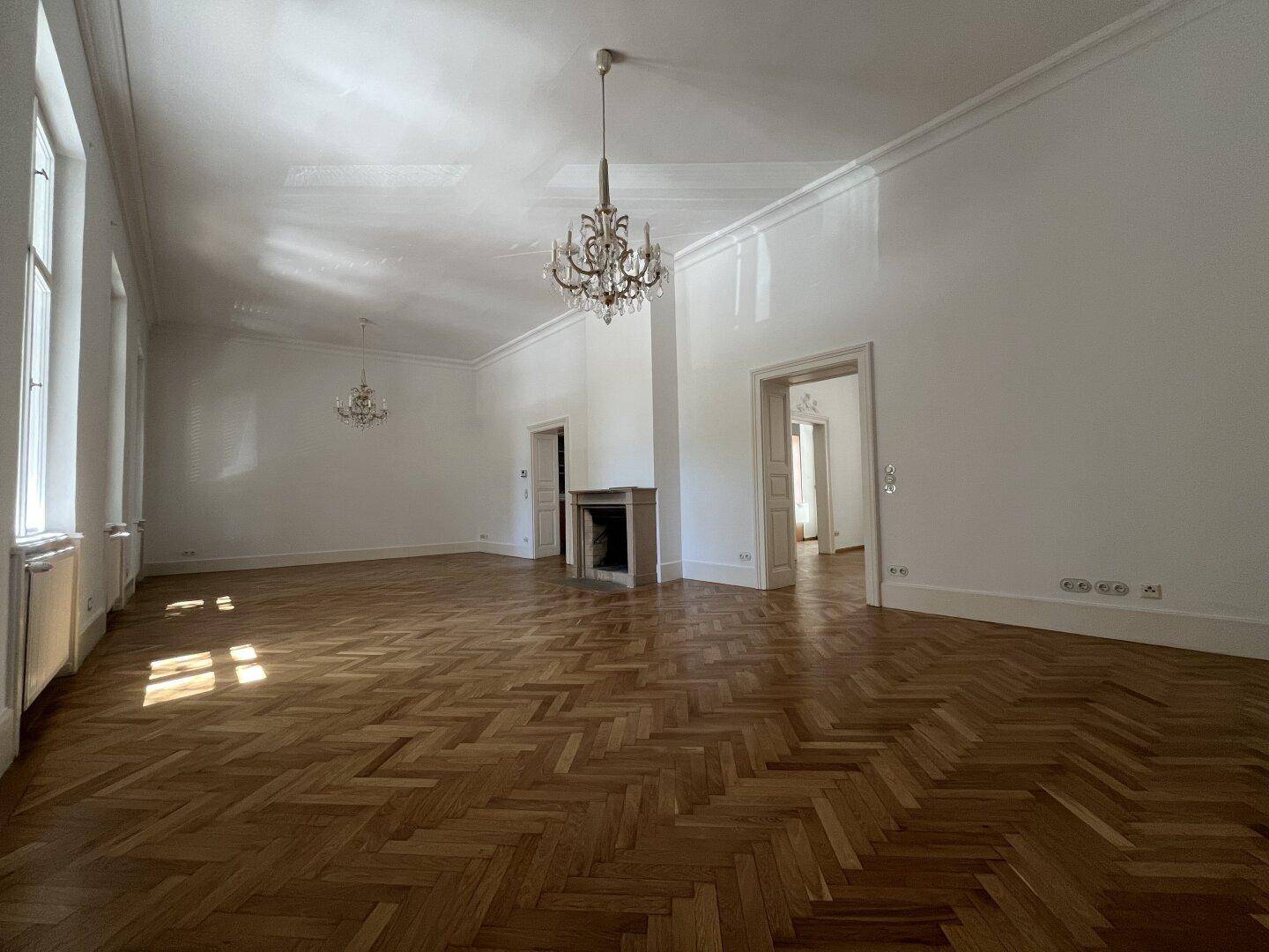 Großes Wohnzimmer mit Fischgrätparkett, Kamin und hohen Decken, ideal für Empfänge.