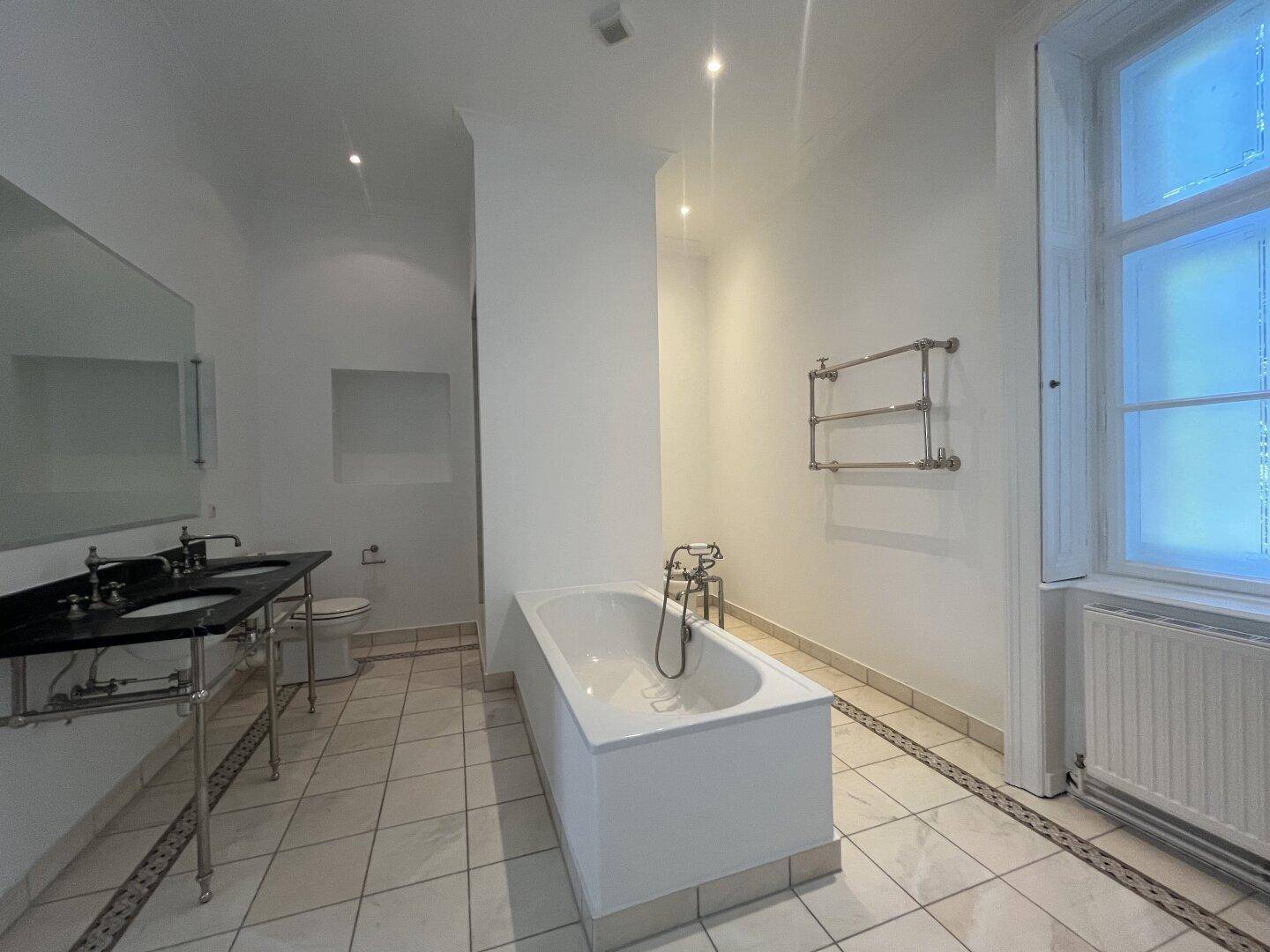 Helles Badezimmer mit Badewanne, Doppelwaschbecken und Fliesenboden.