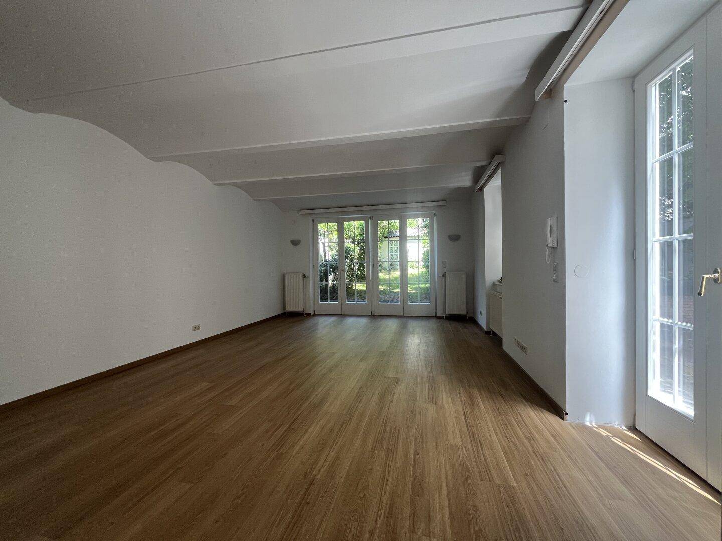 Helles Wohnzimmer mit Holzboden und Zugang zum Garten durch große Fenstertüren.