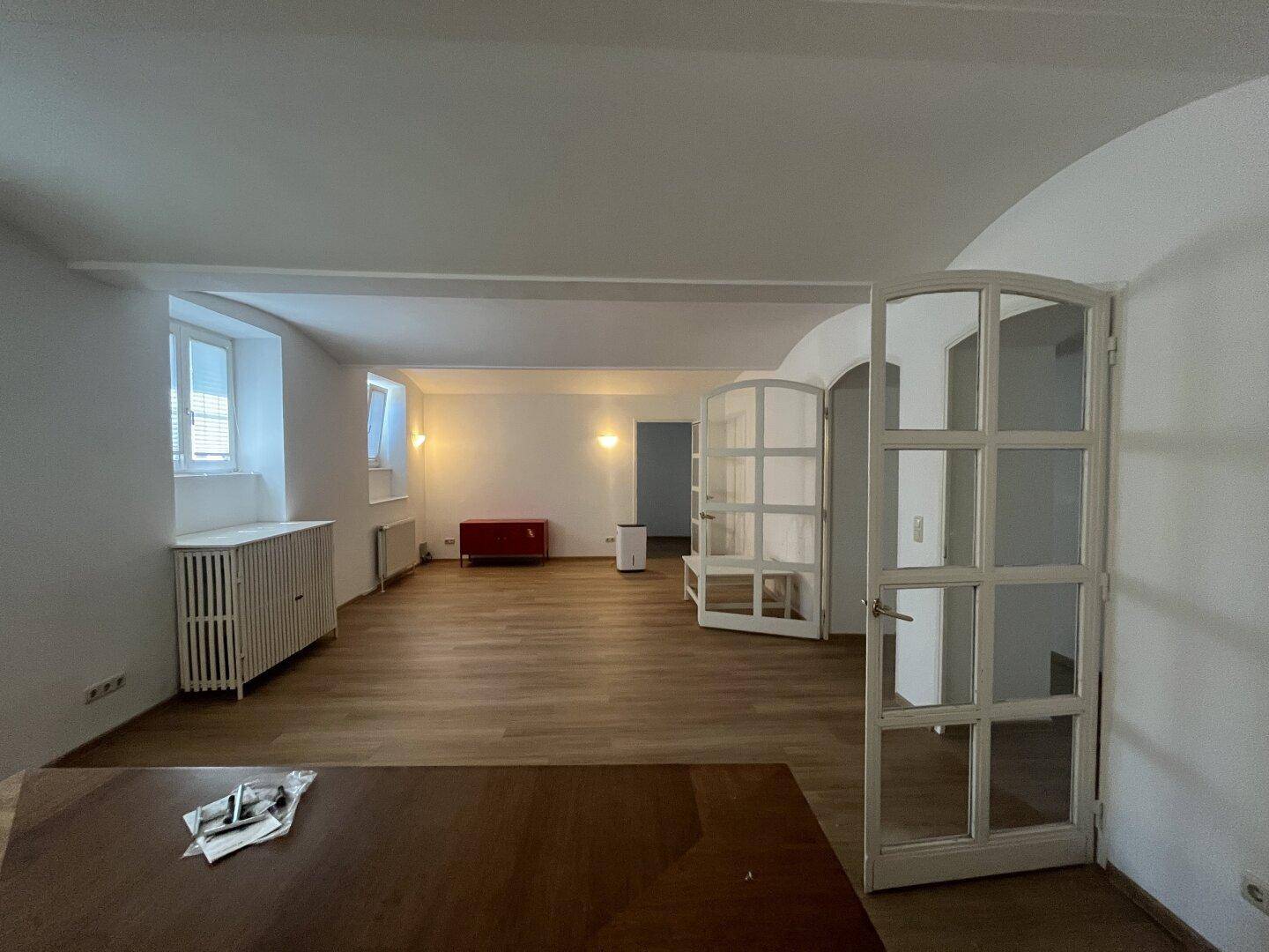 Vielseitiger Raum mit Holzboden und Fenstern, der als Wohn- oder Essbereich genutzt werden kann.