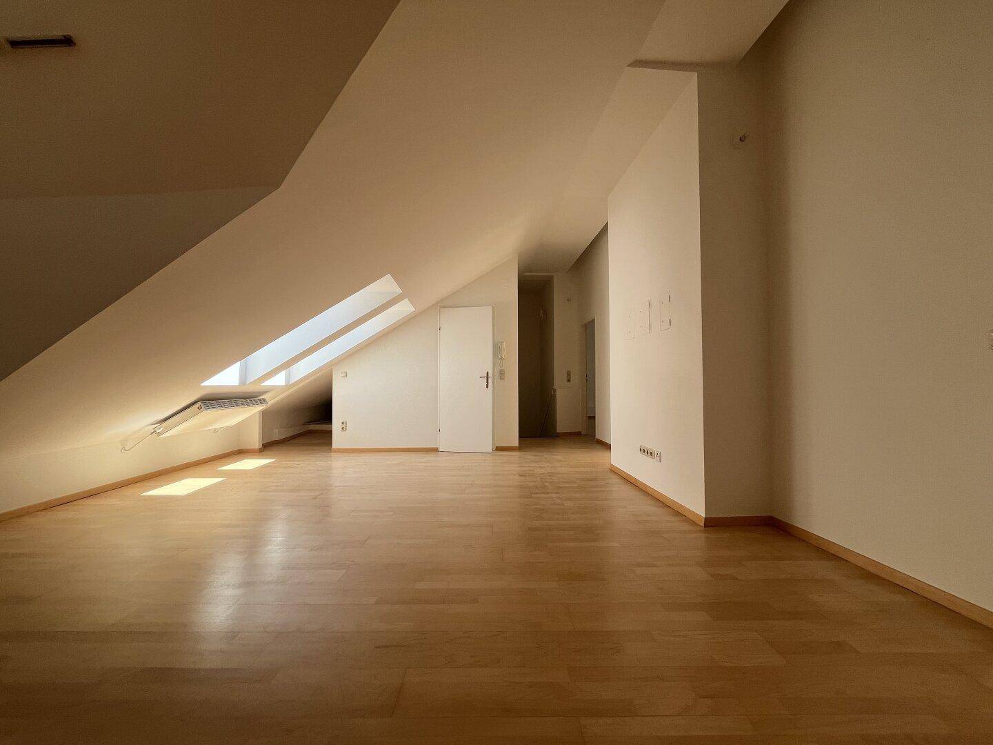 Geräumiger Dachbodenraum mit Holzboden und Dachfenstern, ideal für ein Studio.