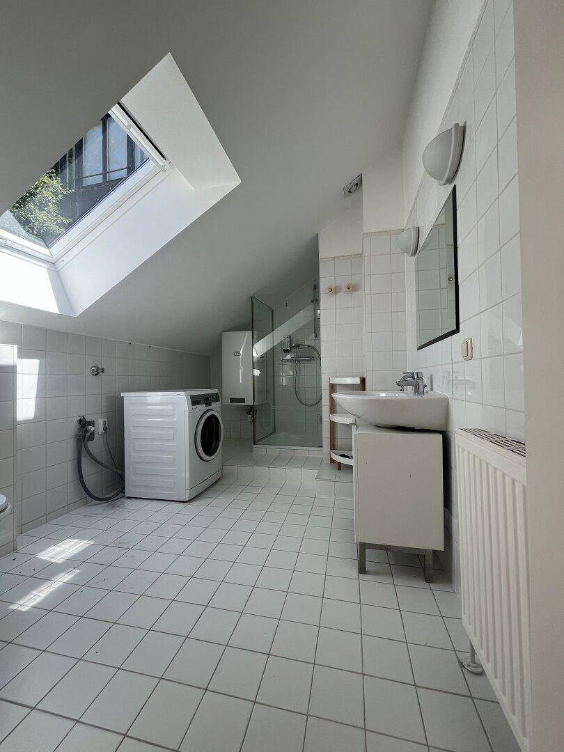 Modernes Badezimmer im Dachgeschoss mit Dusche, Waschmaschine und Dachfenster.