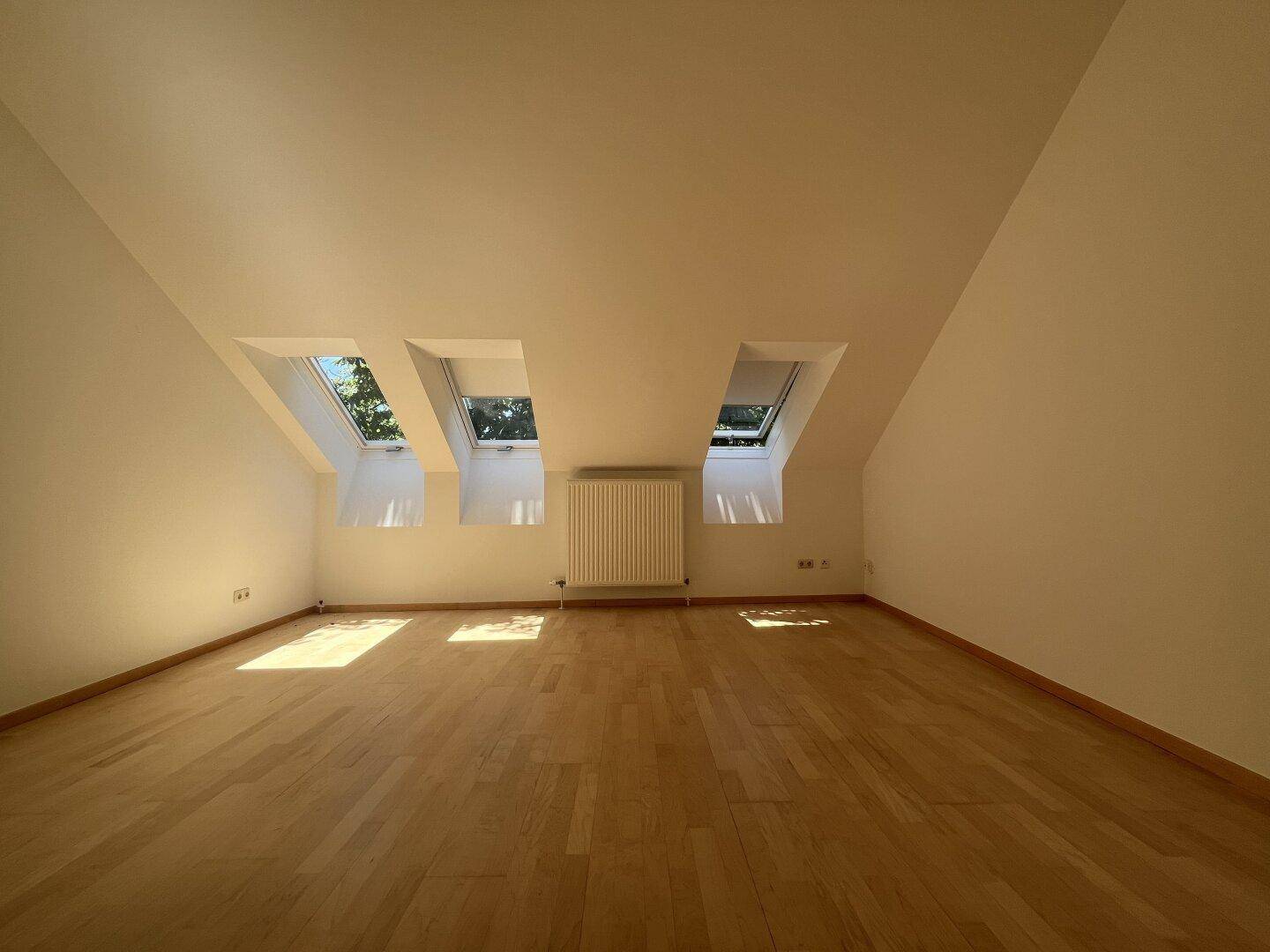 Helles Schlafzimmer im Dachgeschoss mit Holzboden und drei Dachfenstern.