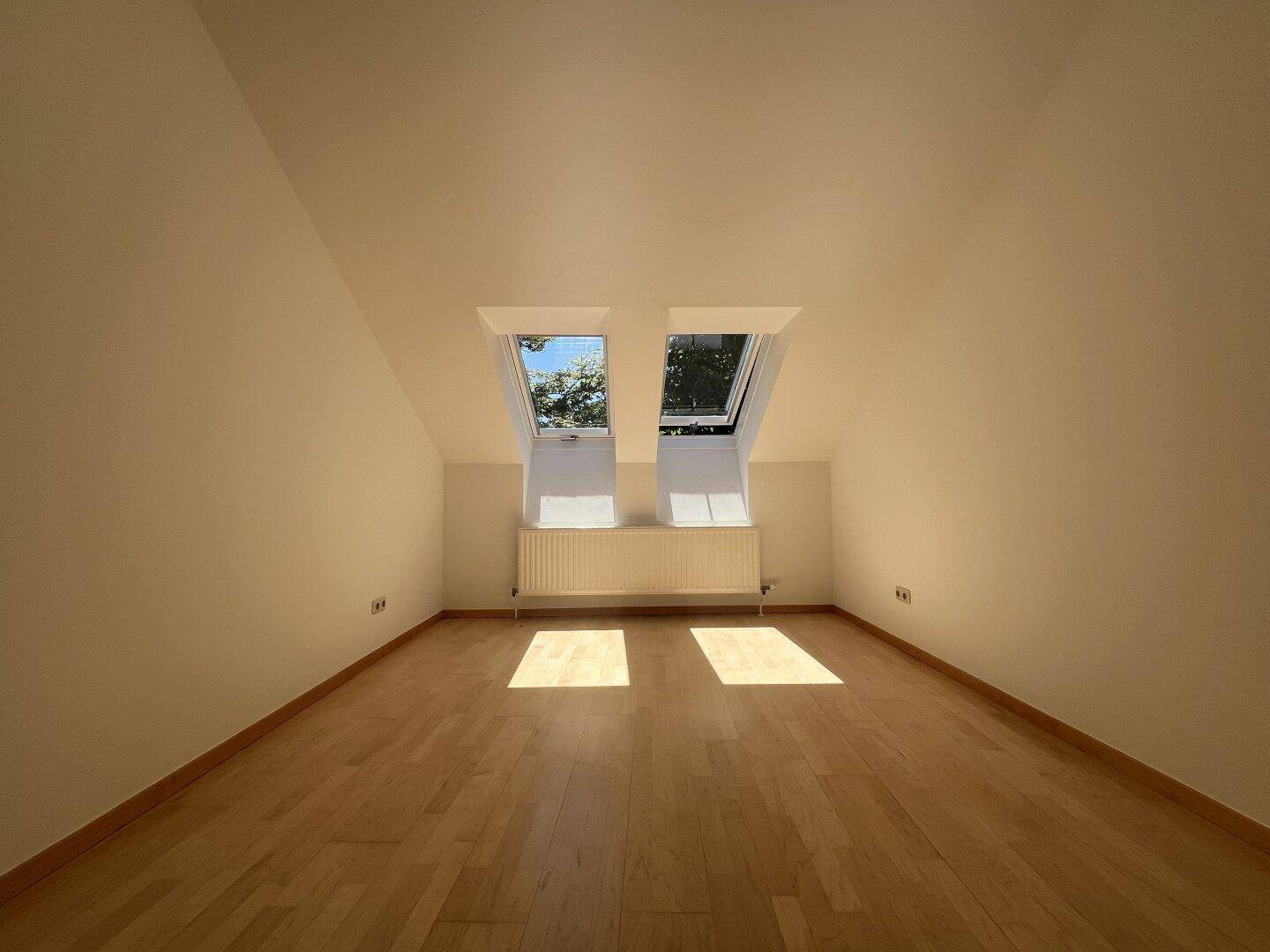 Gemütliches Schlafzimmer im Dachgeschoss mit Holzboden und zwei Dachfenstern.