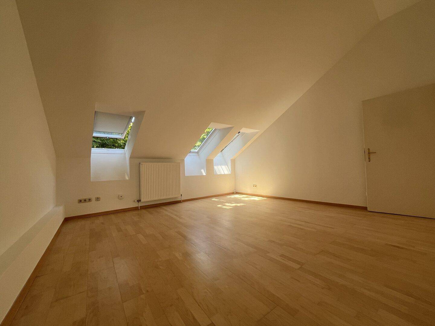 Schlafzimmer im Dachgeschoss mit Holzboden, Dachfenstern und Zugang zu weiteren Räumen.