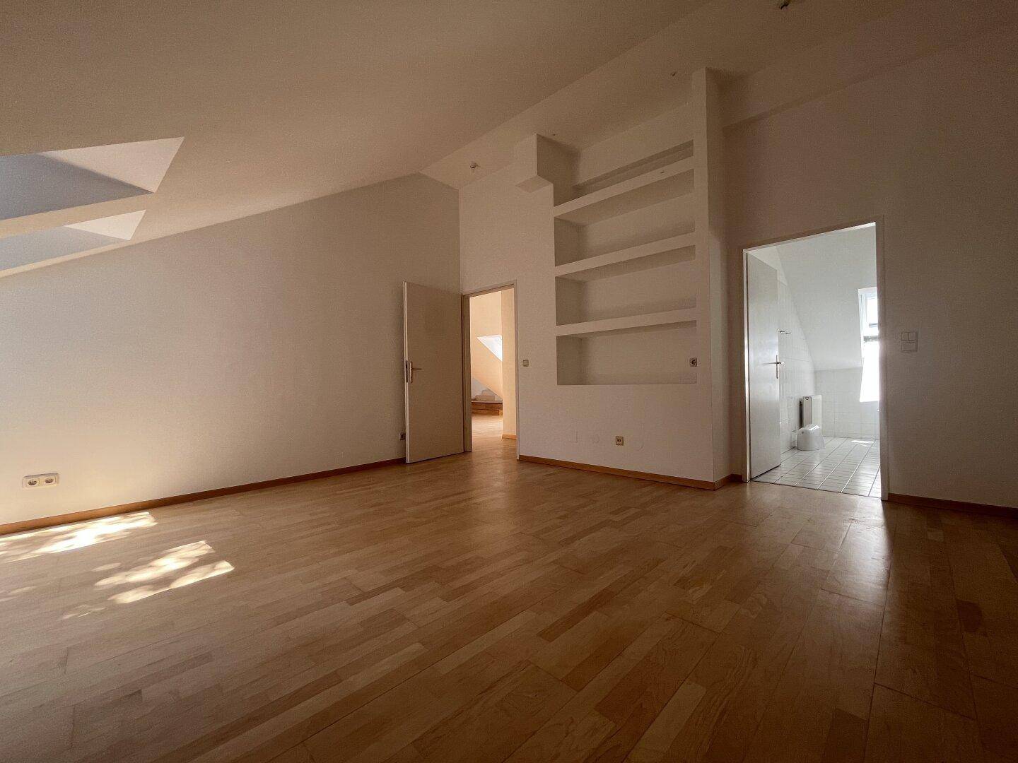 Dachbodenraum mit Holzboden, Einbauregalen und Zugang zu einem Badezimmer.