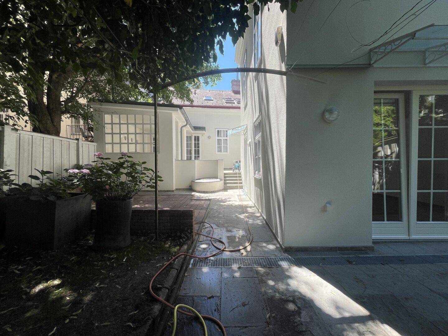 Gepflasterter Terrassenbereich mit Zugang zum Gebäude und angrenzendem grünen Garten.