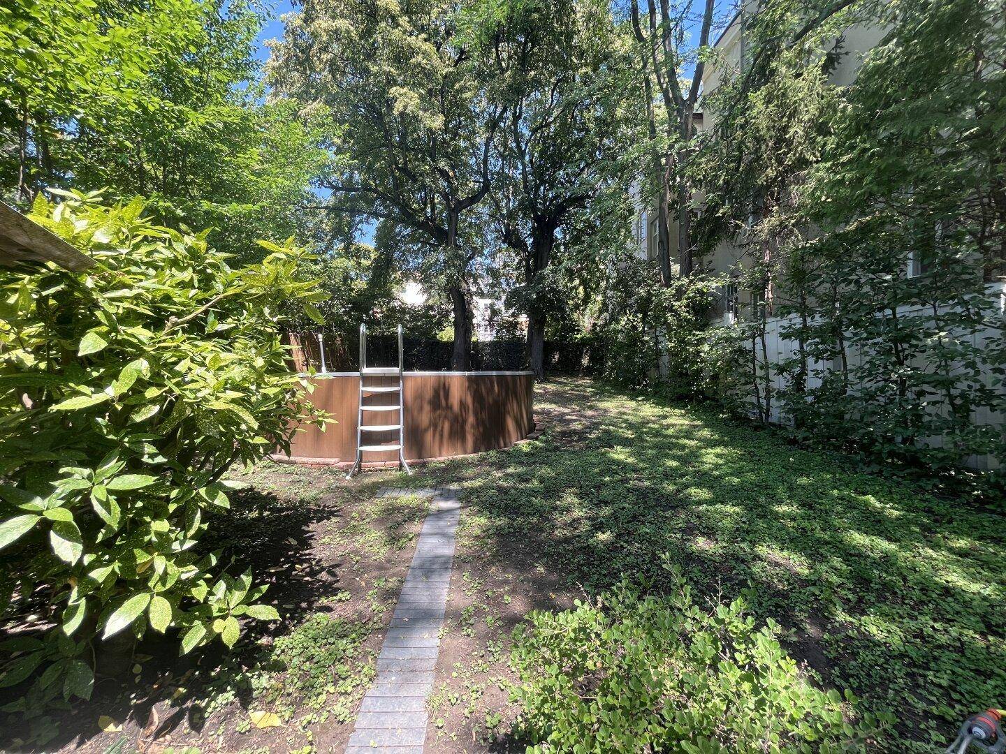 Großer, sonniger Garten mit einem oberirdischen Pool, umgeben von viel Grün und Bäumen.