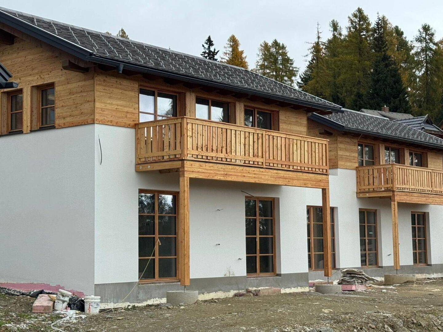 Zwei im Bau befindliche Häuser mit Holzfassaden, weißen Wänden und traditionellen Holzbalkonen.