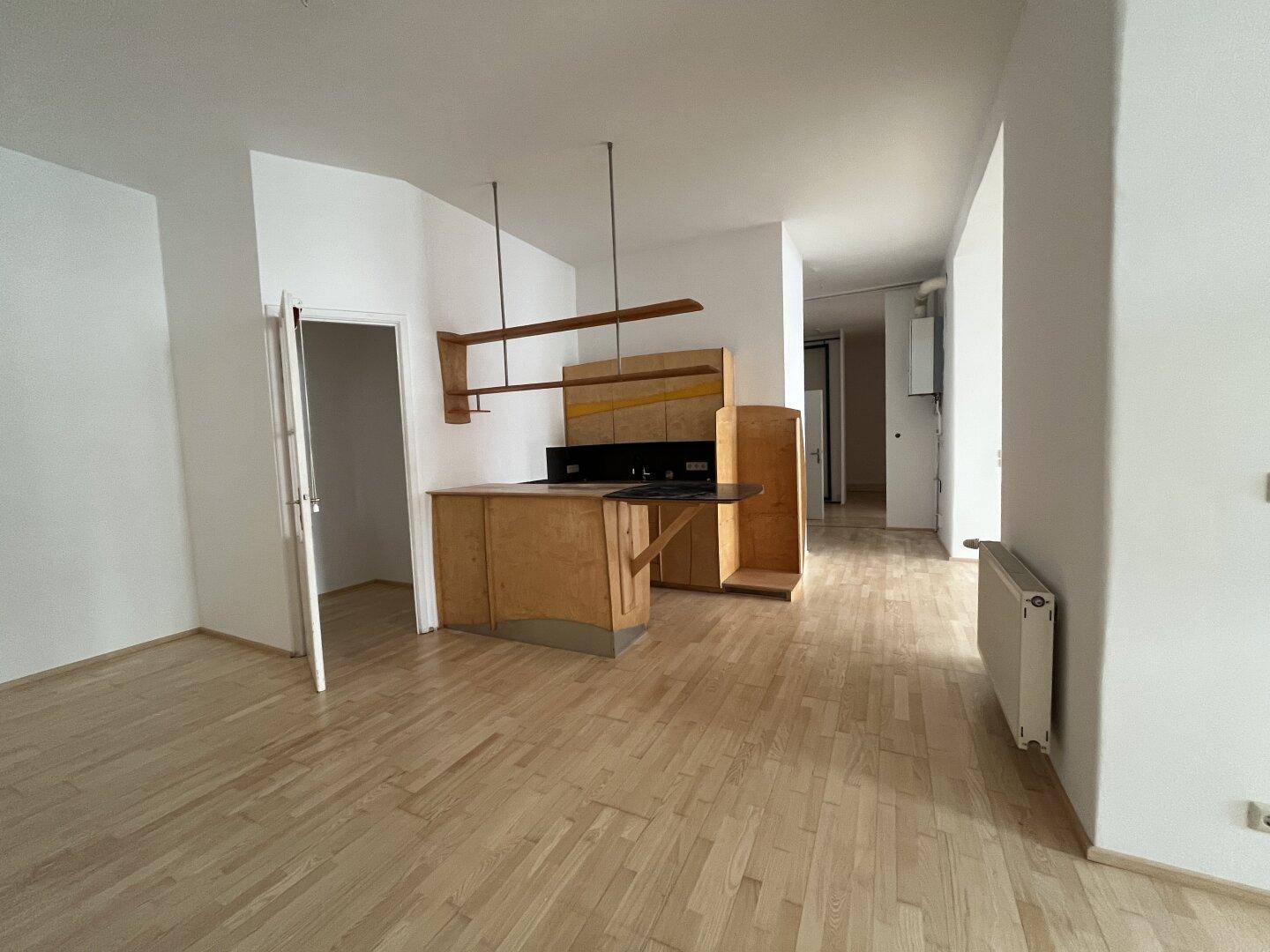 Offener Bereich mit einer einfachen Küchenzeile und glänzendem Holzboden.