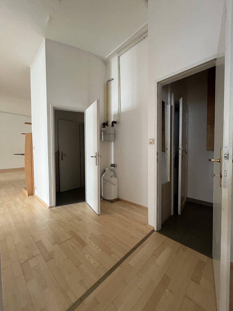 Heller Flur mit Holzboden, mehreren Türen und sichtbaren Versorgungsleitungen.
