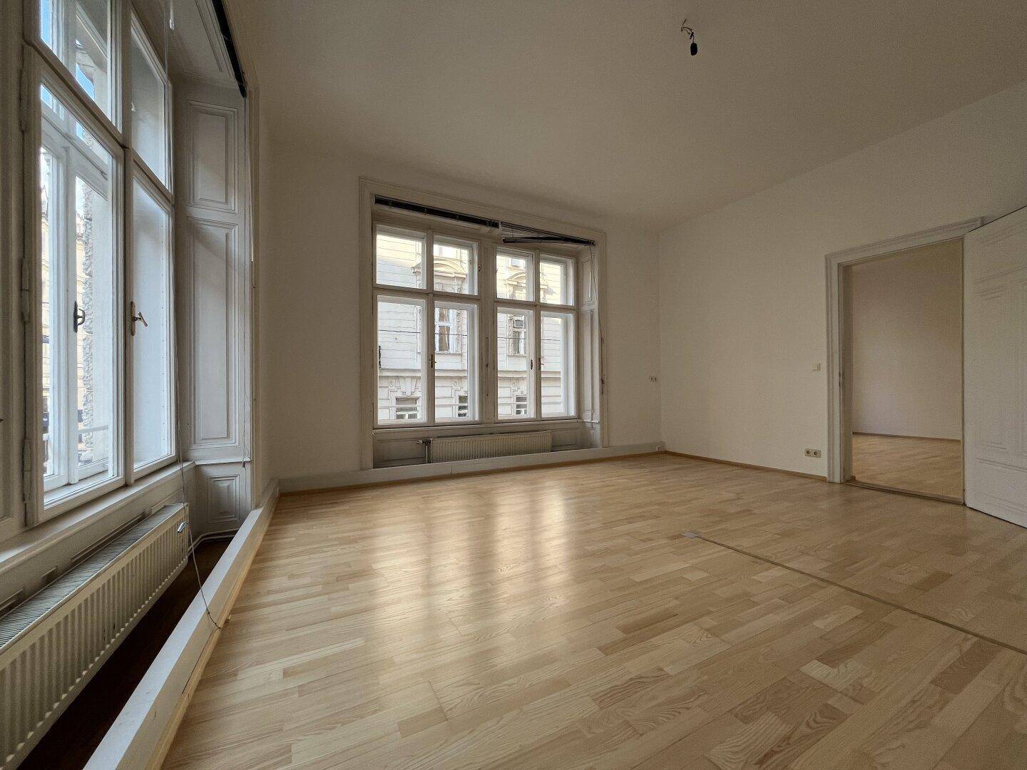 Heller Wohnraum mit Erkerfenster, Holzboden und Blick auf die Straße.