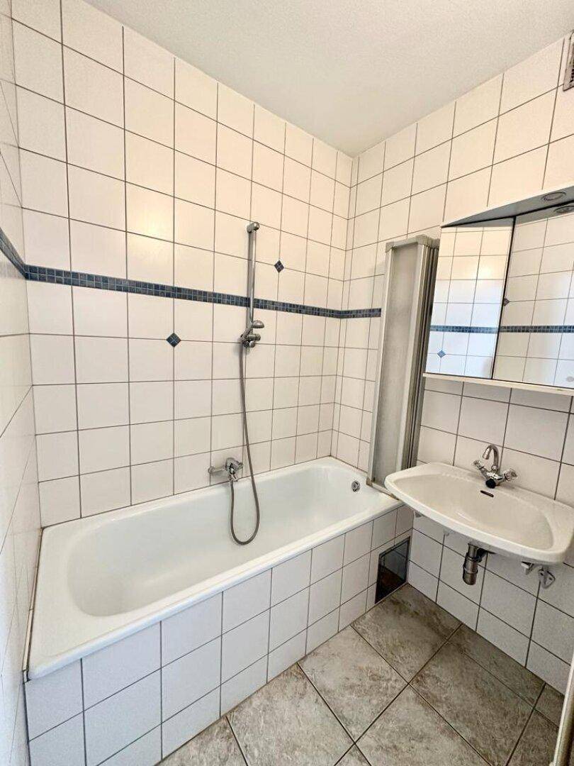 Badezimmer mit Badewanne, Duschfunktion, Waschbecken und Spiegelschrank in weiß-blauer Fliesengestaltung.