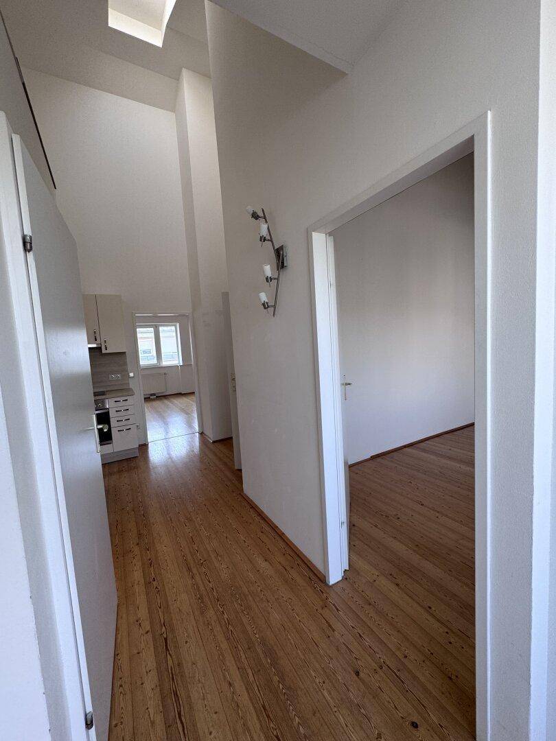 Heller Flur mit Holzdielenboden und hohen Decken, der zu den verschiedenen Zimmern der Wohnung führt.