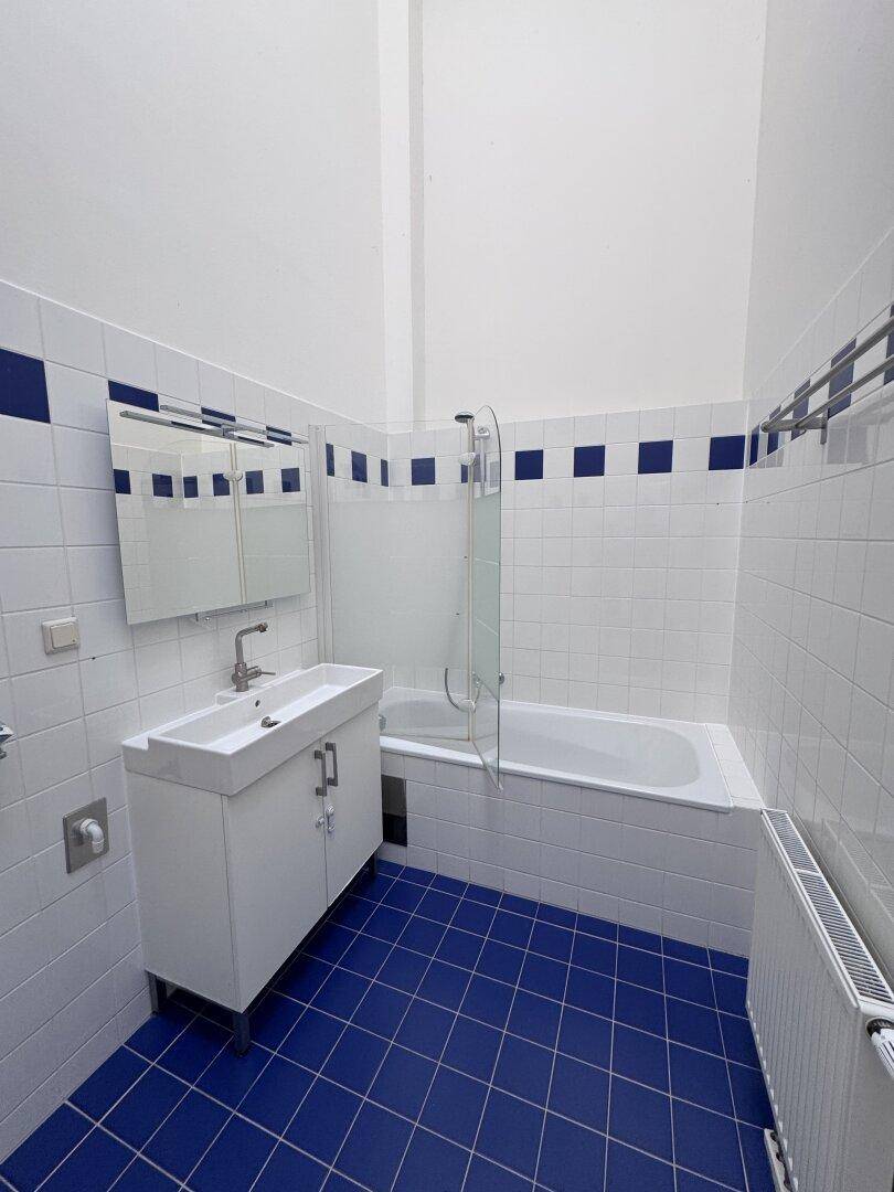 Badezimmer mit blauen und weißen Fliesen, Badewanne mit Duschwand und modernem Waschtisch.