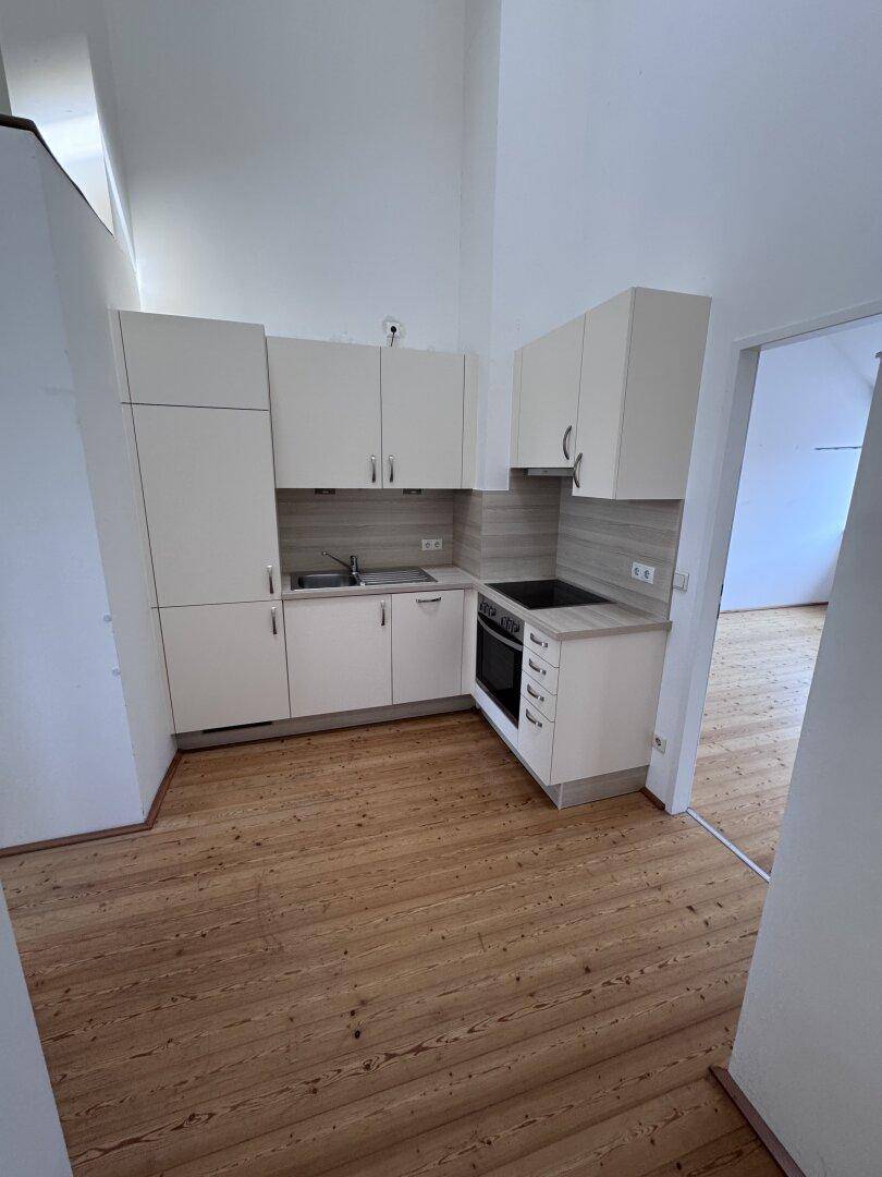 Kompakte Einbauküche mit weißen Schränken, Herd und Spüle, integriert in einen hellen Raum mit Holzboden.
