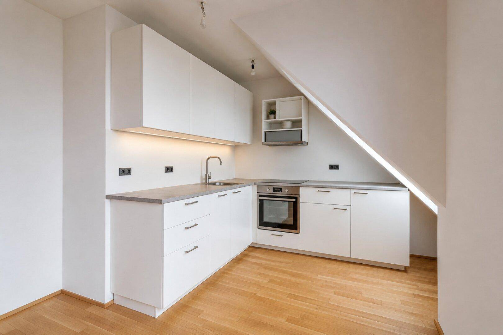 Moderne Einbauküche in Weiß mit Dachschräge und Holzfußboden, ideal für eine Dachgeschosswohnung.