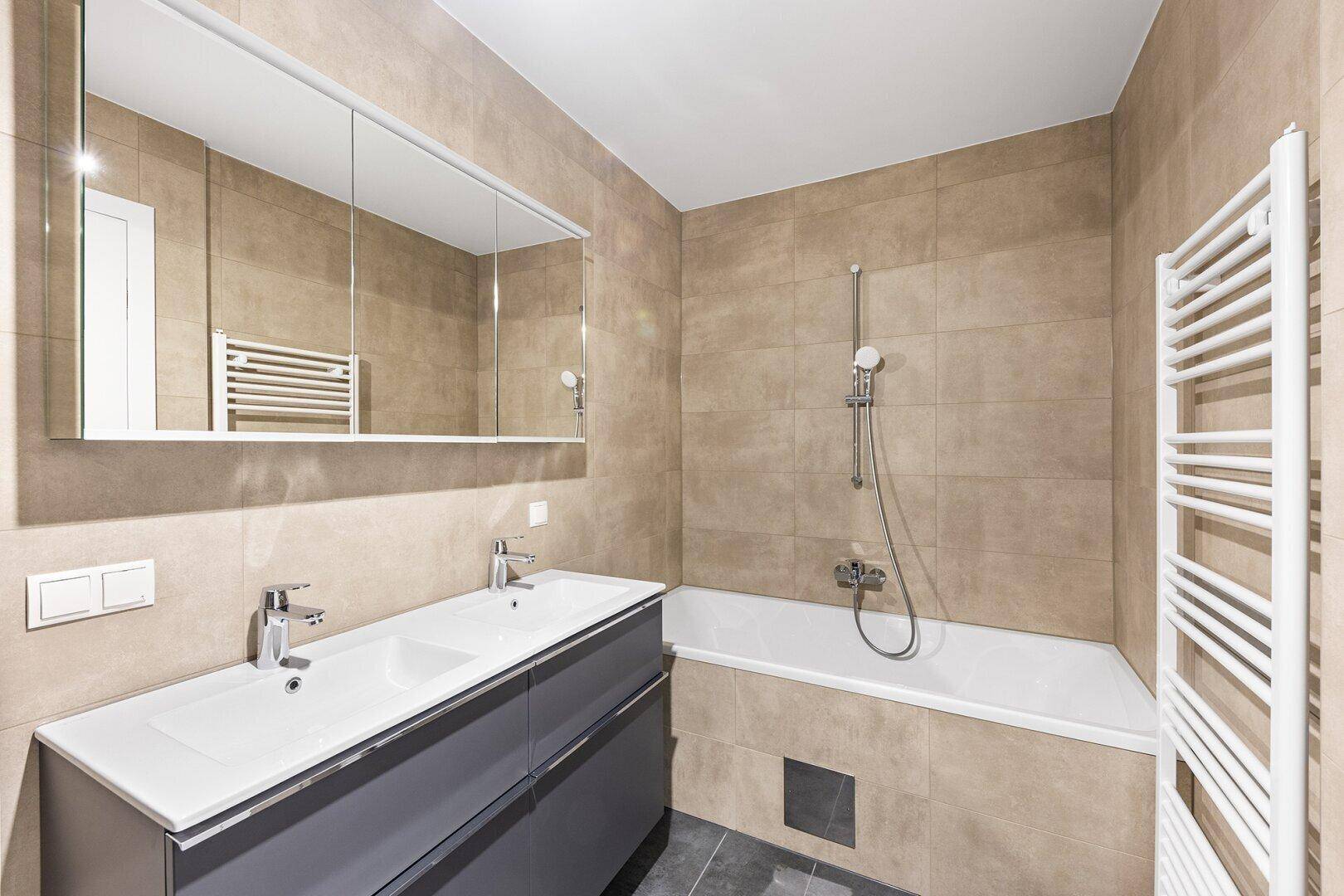 Helles Badezimmer mit Badewanne, Doppelwaschbecken und beheiztem Handtuchhalter.