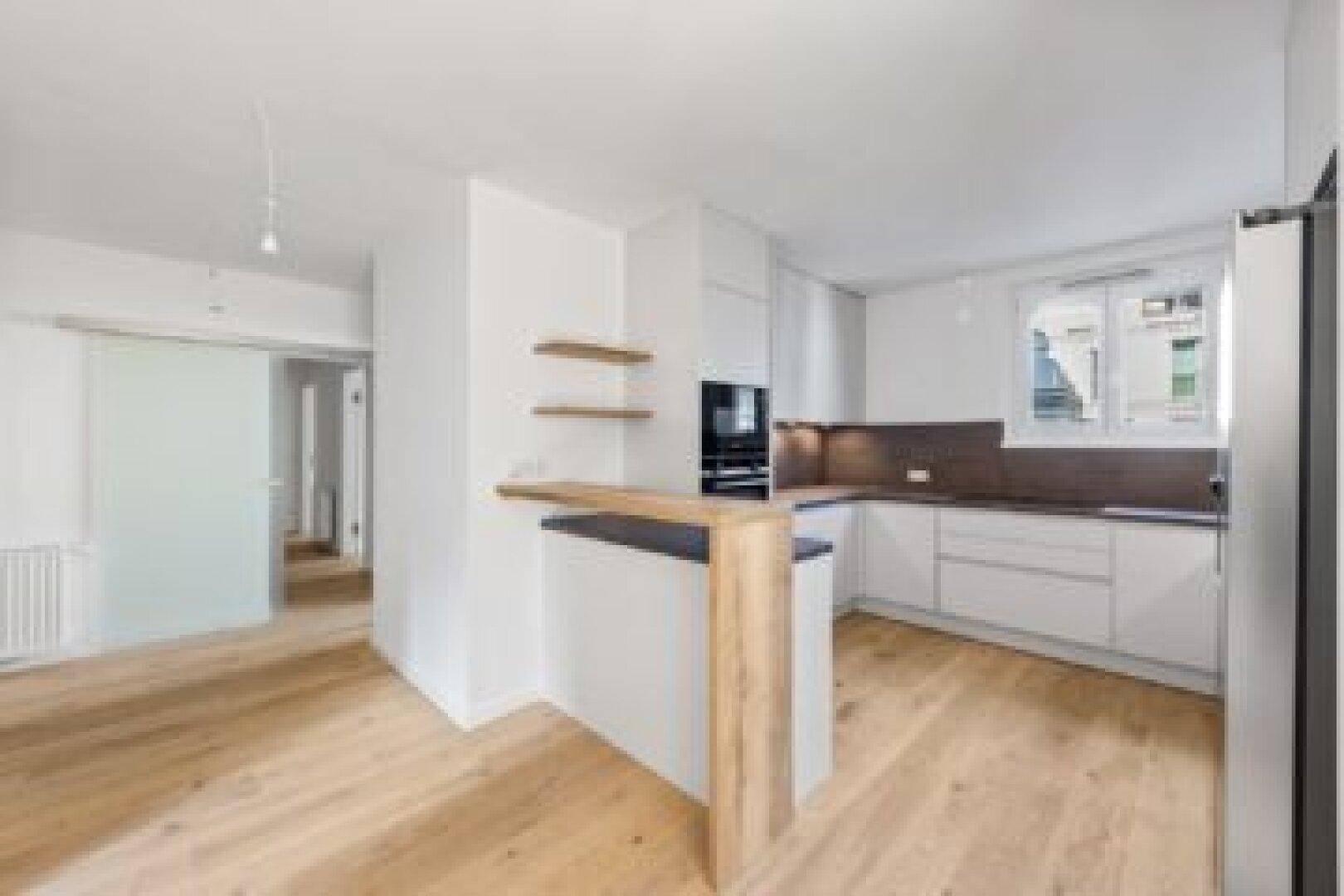 Offene Küche mit Frühstücksbar, weißen Schränken und Holzboden.