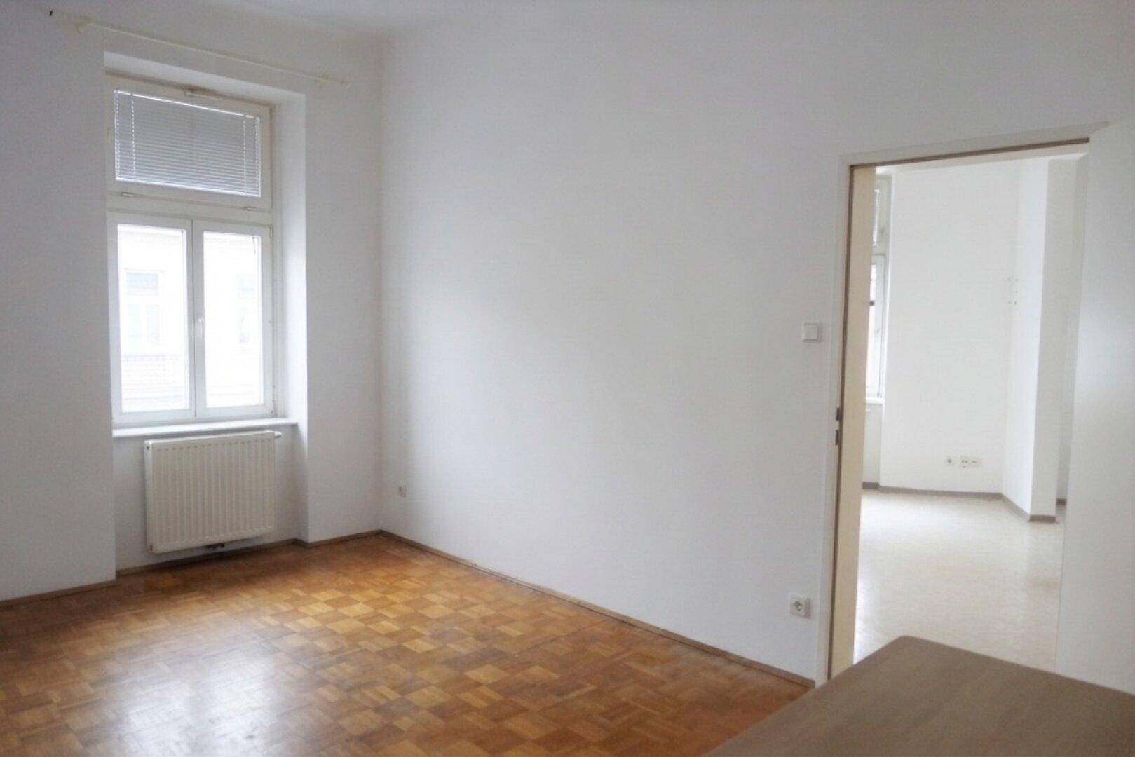 Heller Raum mit Parkettboden und offener Tür zu weiteren Zimmern, bereit zur individuellen Gestaltung.