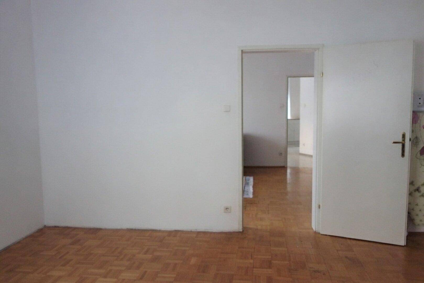 Geräumiges Zimmer mit Parkettboden und offener Tür zu einem weiteren Wohnbereich, vielseitig nutzbar.