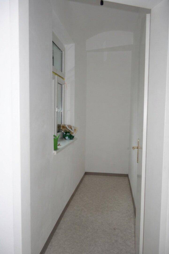 Schmaler Flur mit Fenster, das für natürliche Belichtung sorgt und den Raum aufhellt.