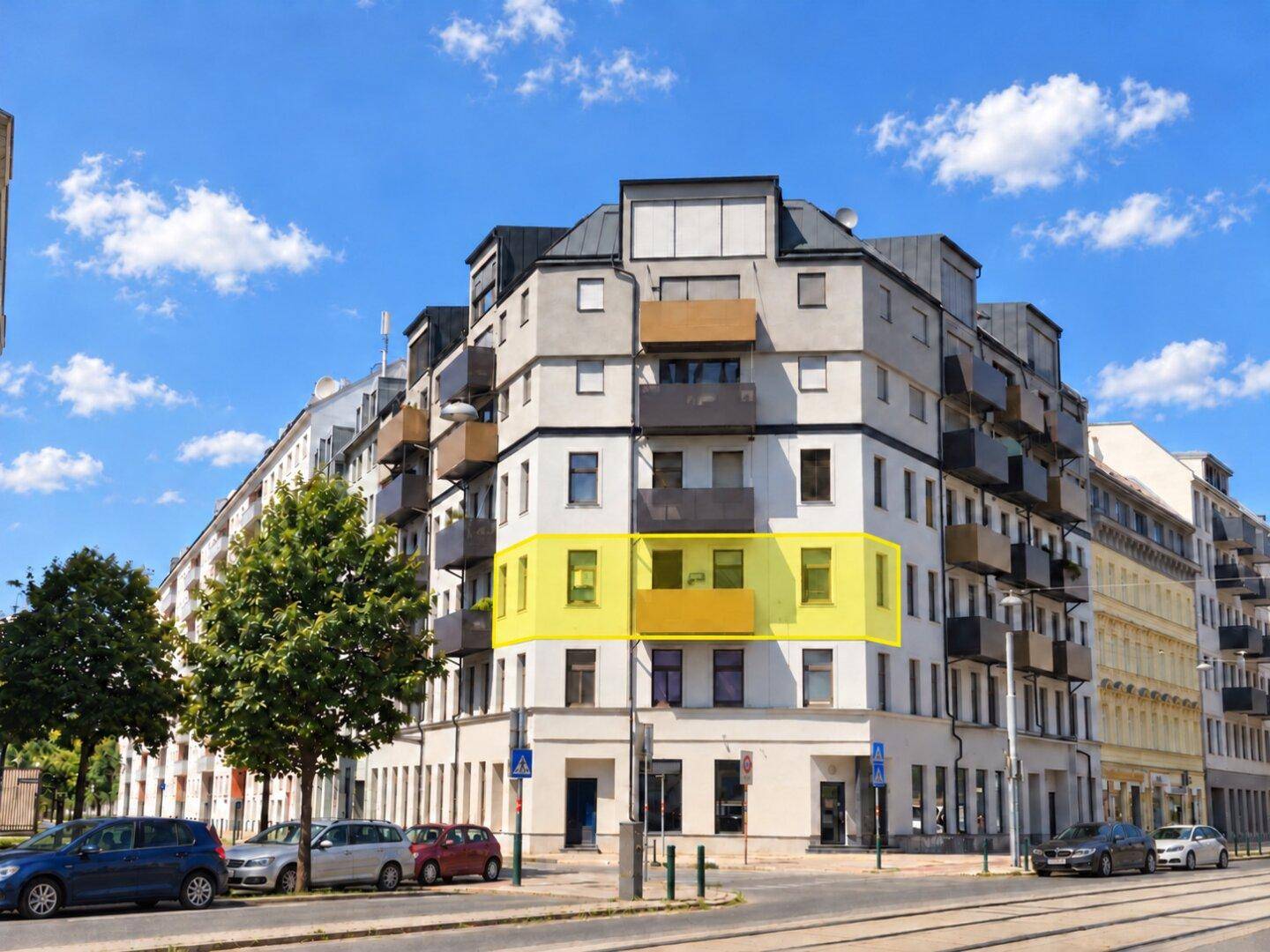 Modernes Wohngebäude mit hervorgehobener Balkonpartie und städtischer Umgebung unter blauem Himmel.