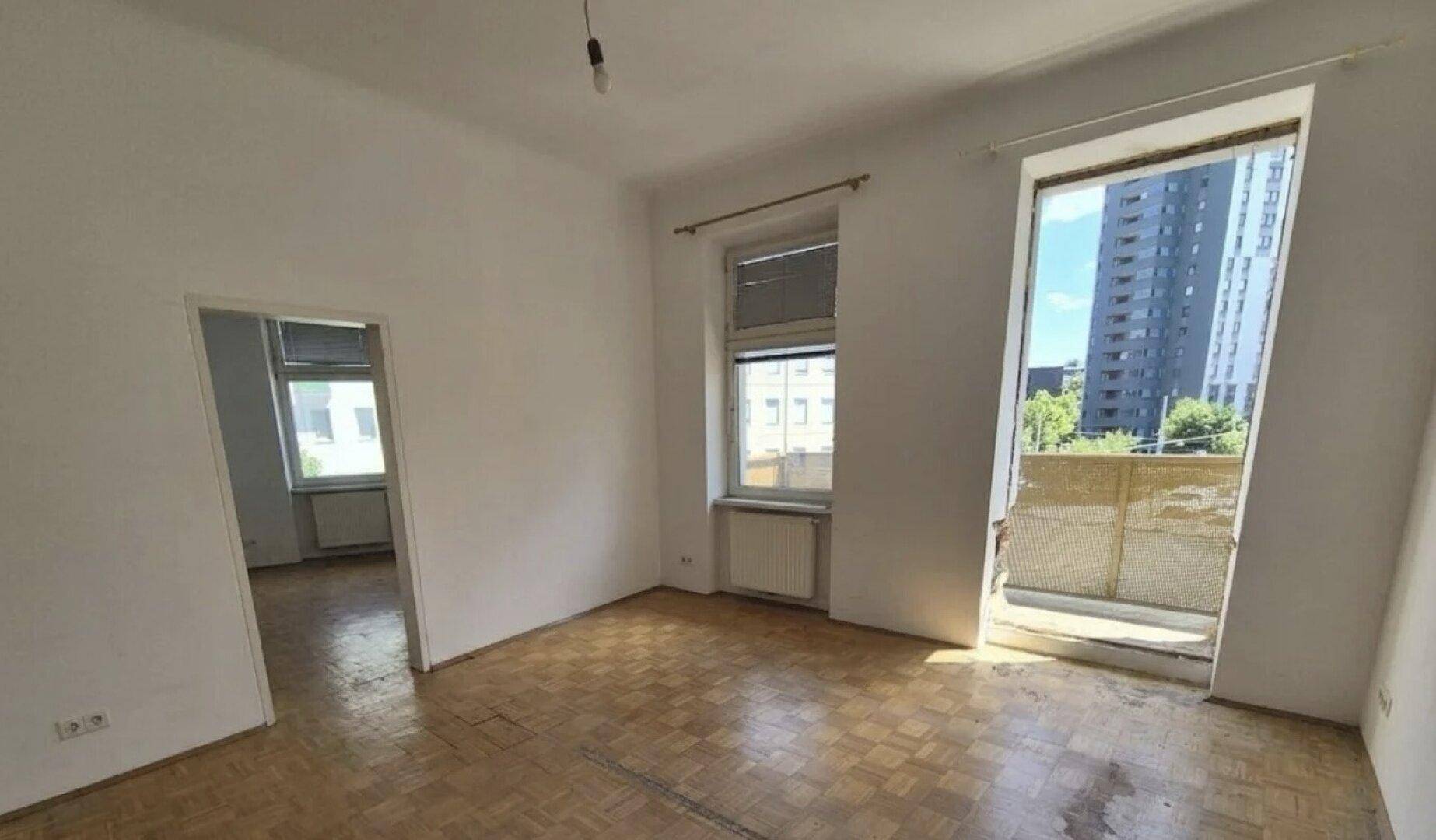 Helles Zimmer mit Fischgrätparkett und Zugang zu einem französischen Balkon, bereit zur Gestaltung.