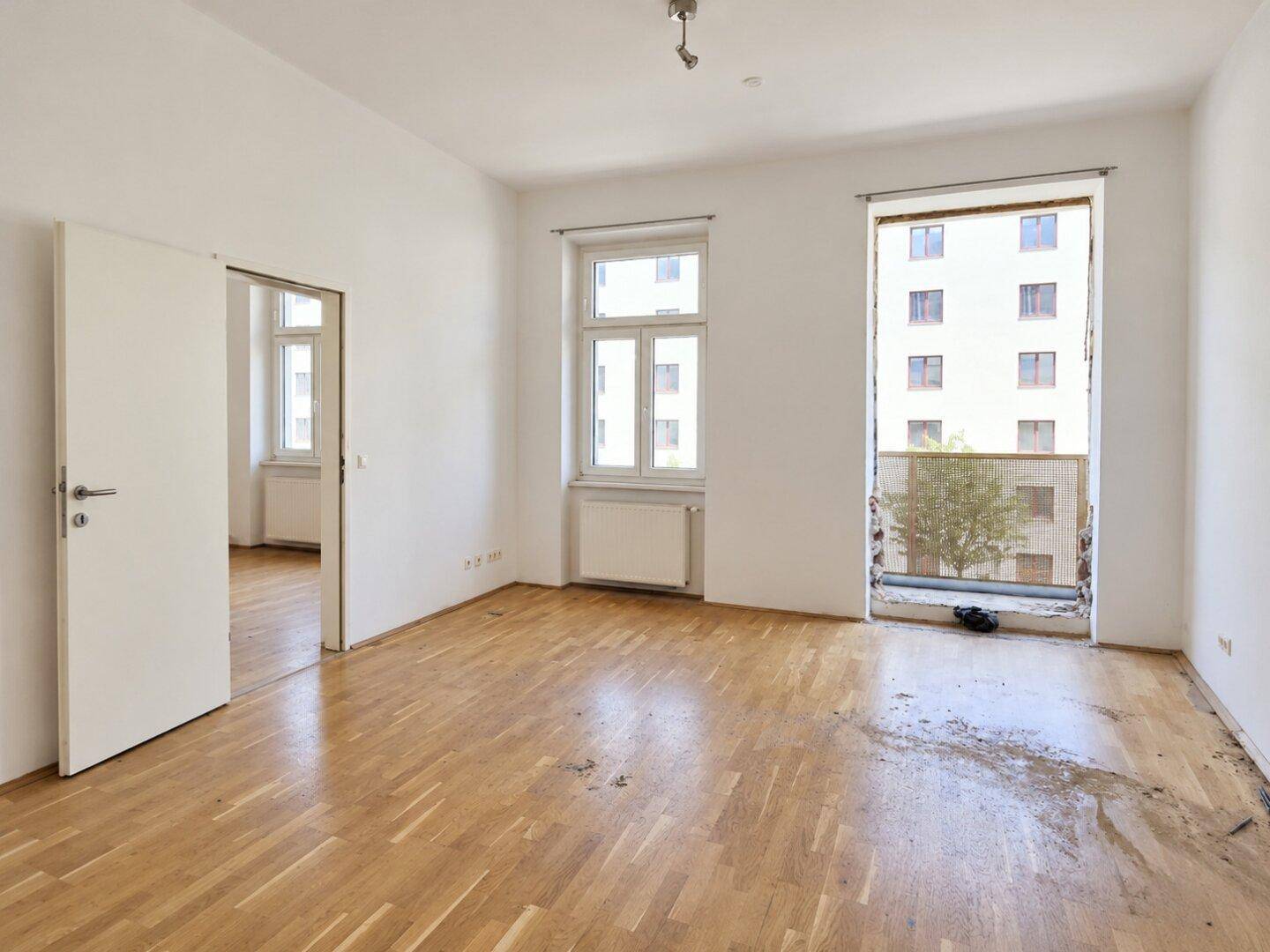 Helles, leeres Zimmer mit Parkettboden und großen Fenstern, bereit zur individuellen Gestaltung.