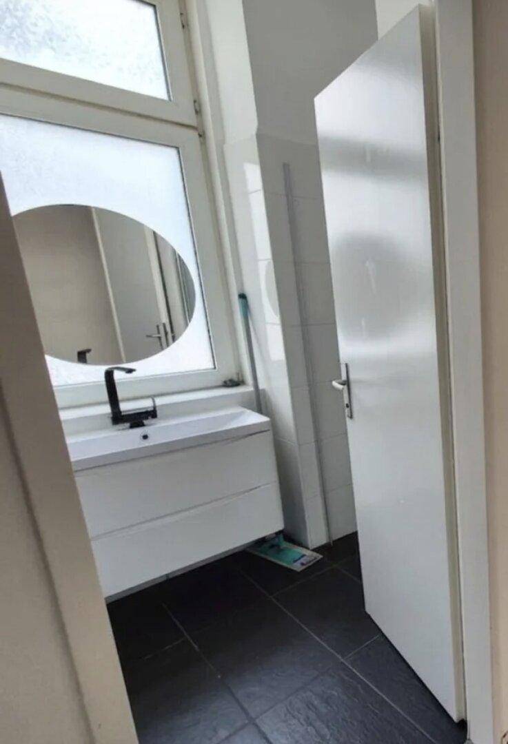 Modernes Badezimmer mit weißem Waschtisch, rundem Spiegel und Fenster für natürliches Licht.