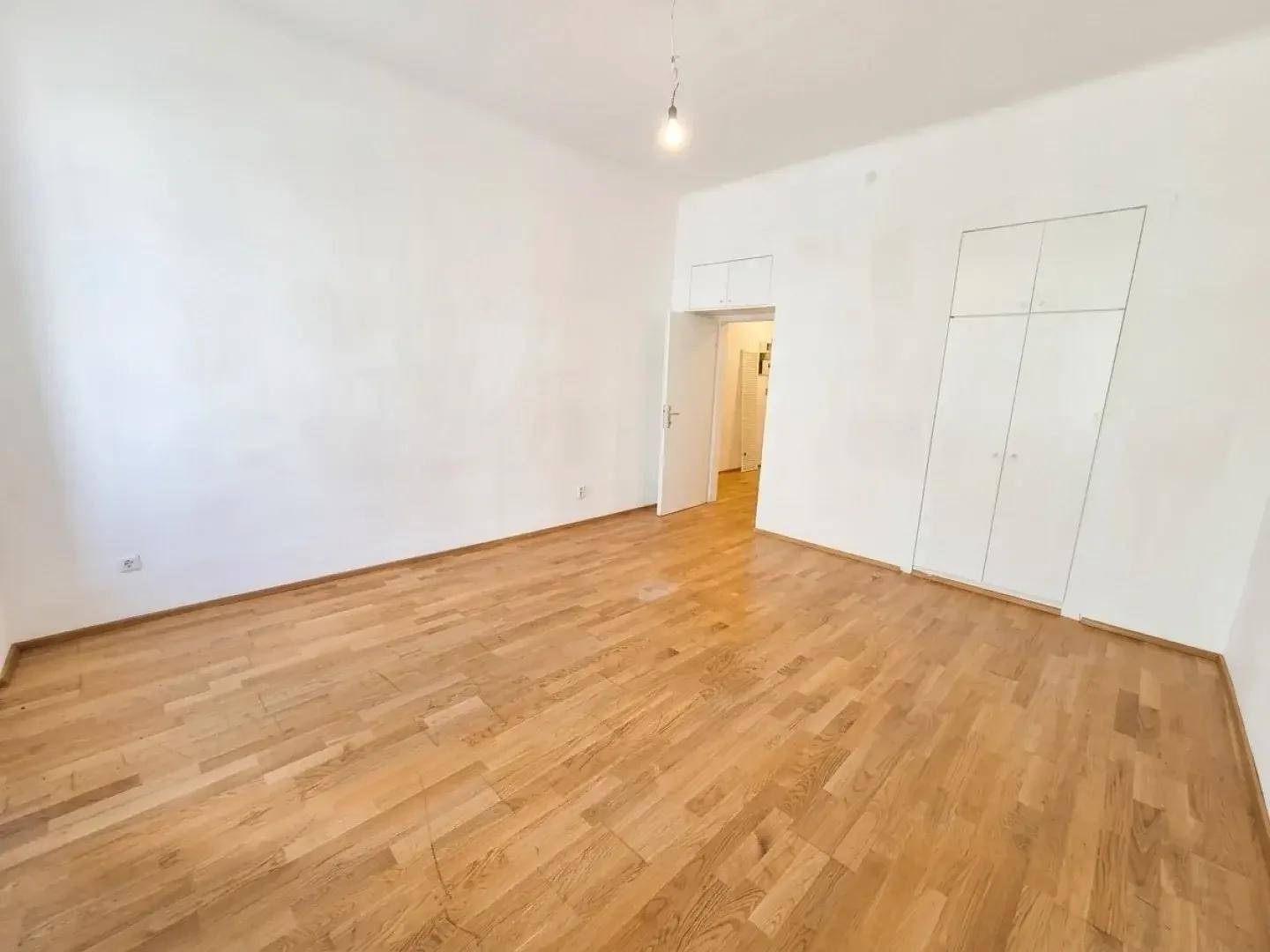 Heller, leerer Raum mit hellem Holzparkettboden und weißen Wänden, inklusive Einbauschränken.